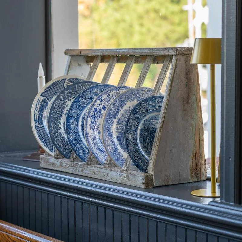 A wooden rack holding several blue and white decorative plates on a windowsill.
