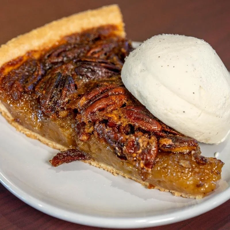 Slice of pecan pie with a scoop of vanilla ice cream.