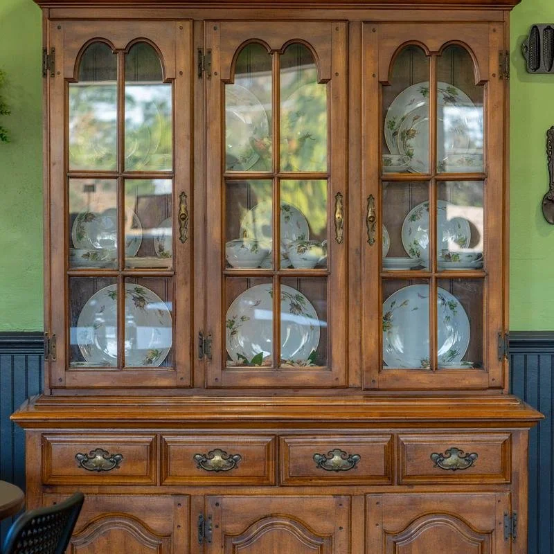 Wooden china cabinet displaying white porcelain dishes with floral patterns in a room with green walls.
