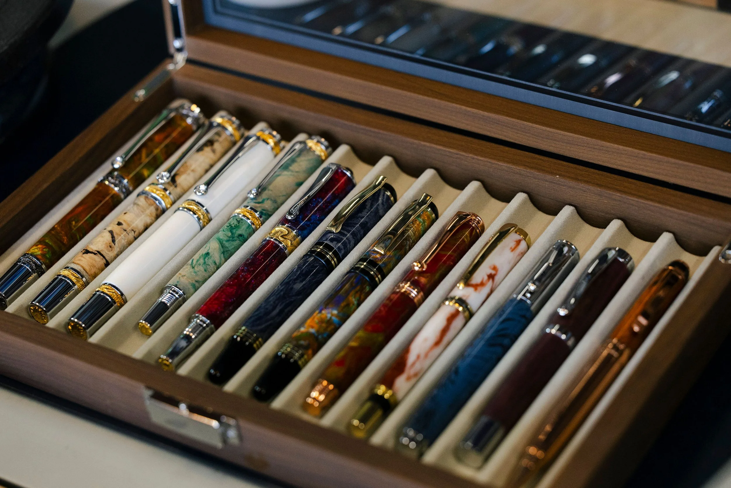 A wooden display case containing various colorful fountain pens with gold accents.