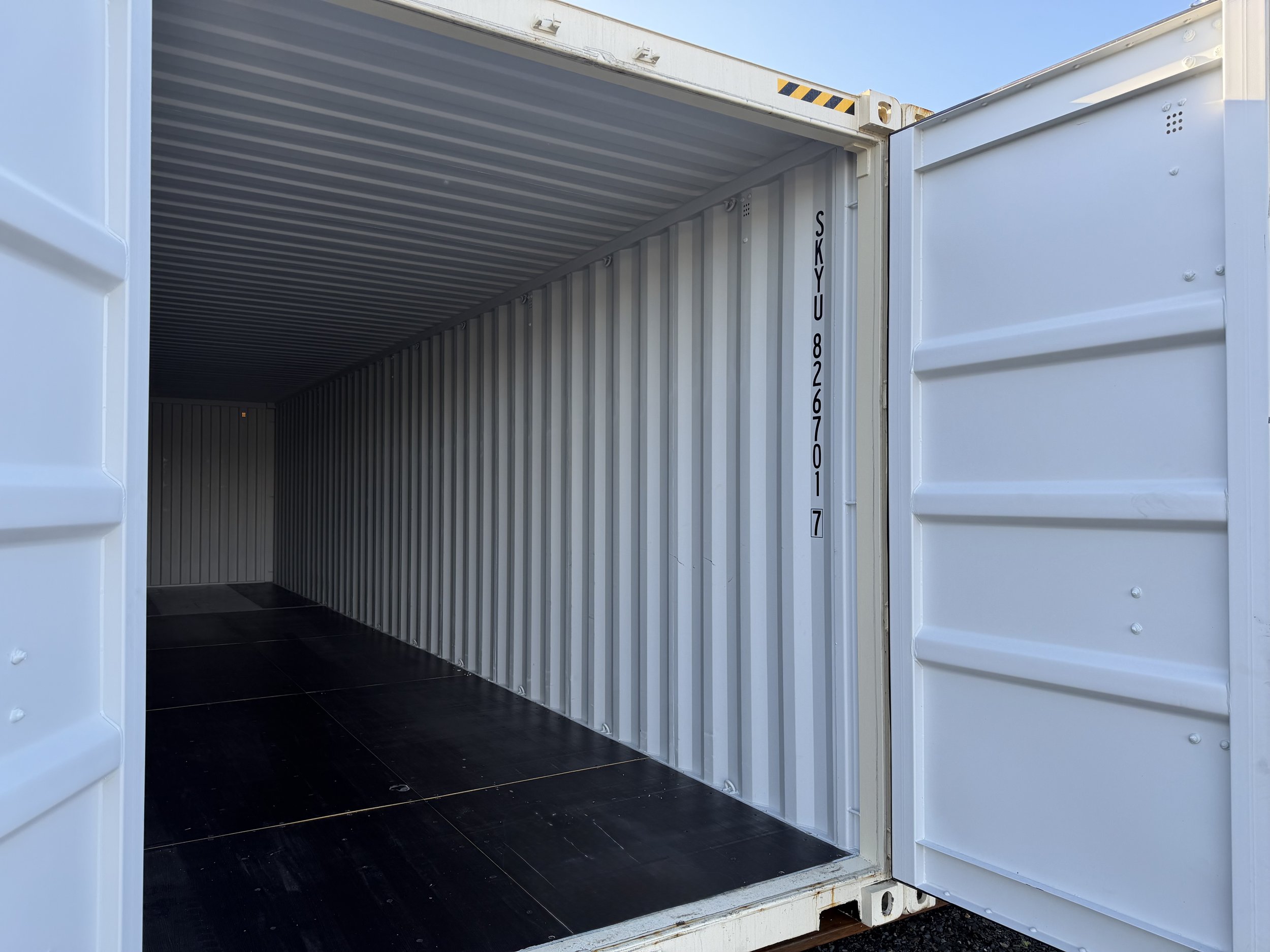 Empty shipping container with open doors, showing metal interior walls and a dark floor.