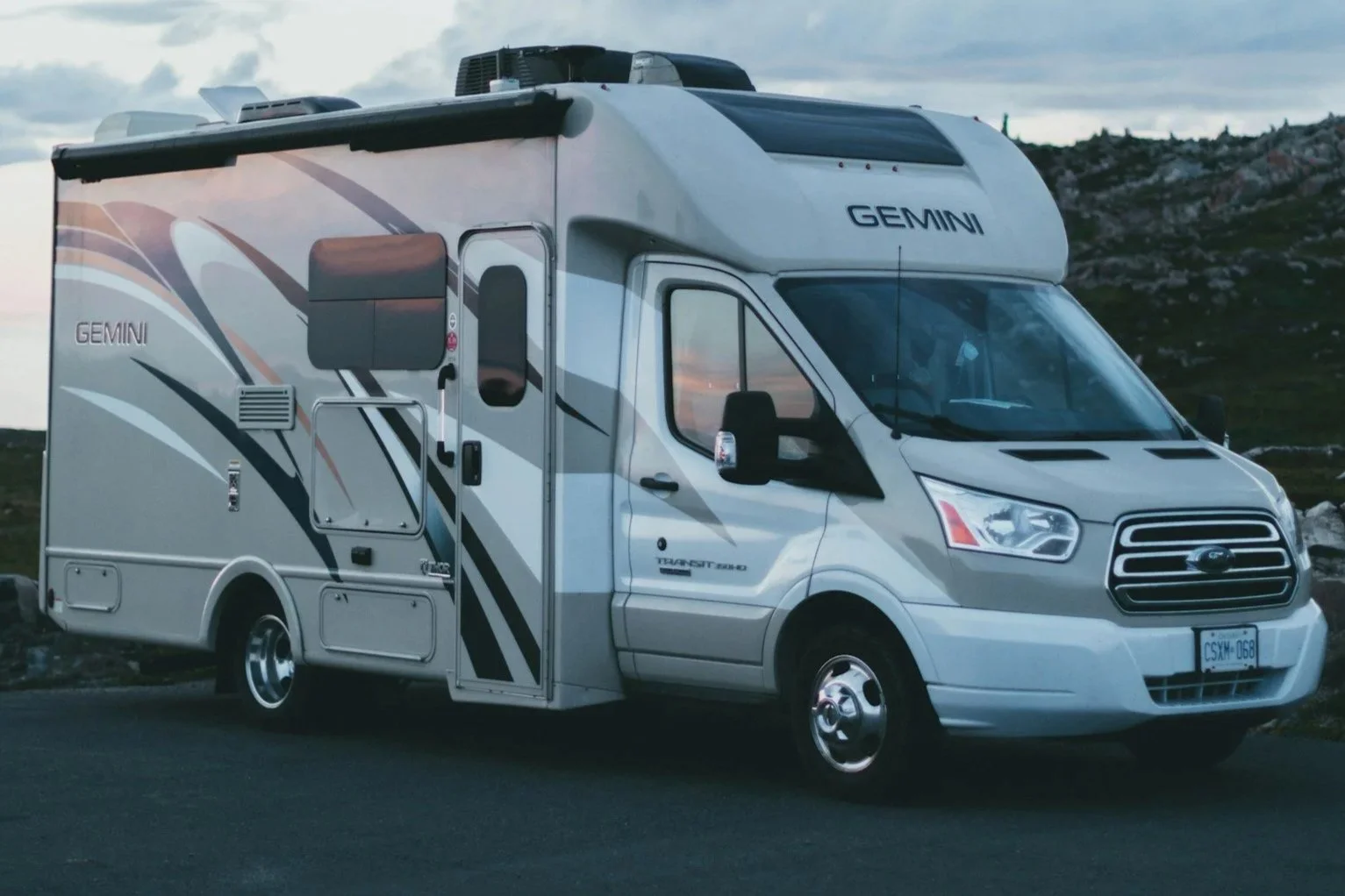 A white Ford camper van with the brand name "GEMINI" on the front and side, parked on a road with hilly terrain in the background.