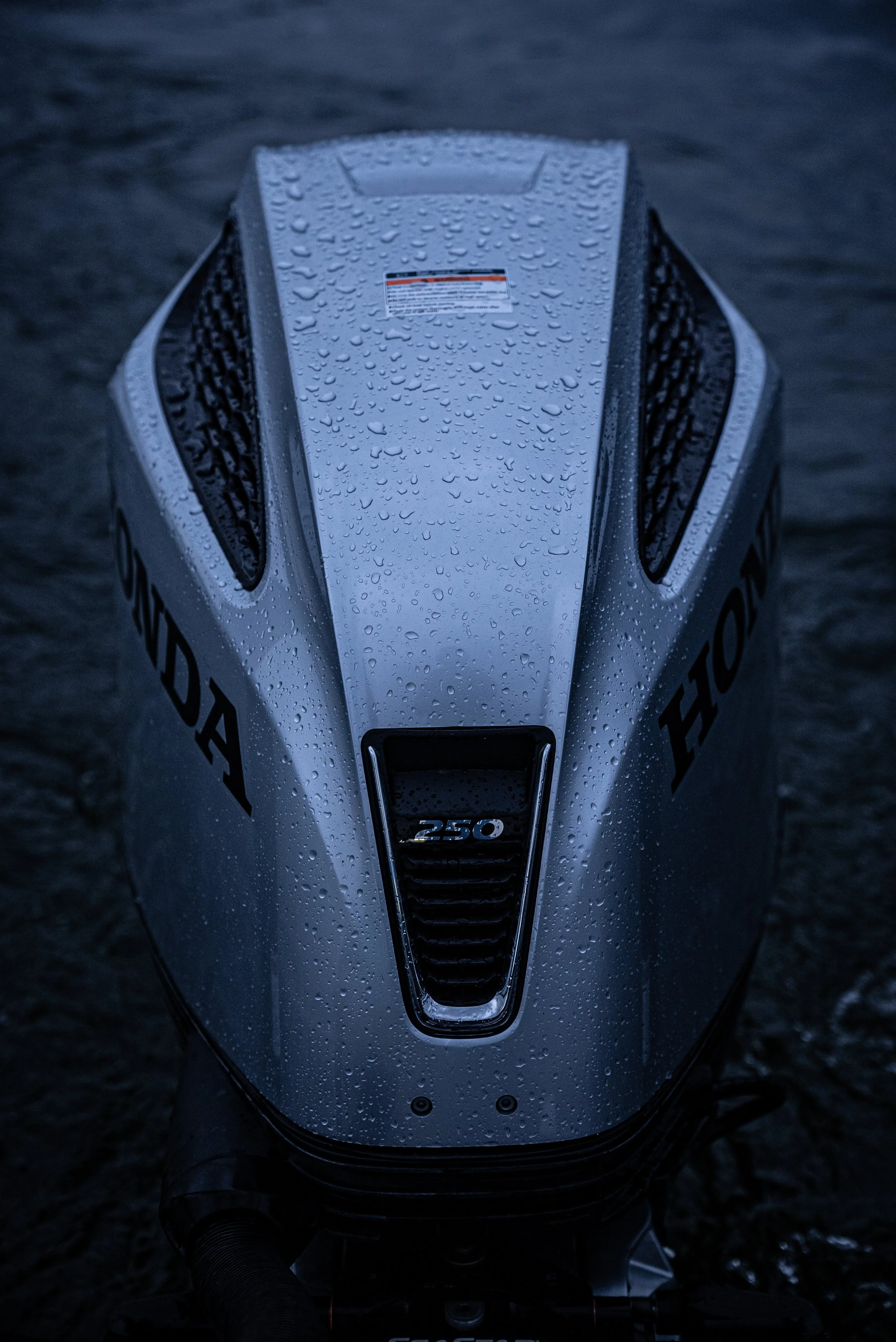 A Honda outboard motor with a 250 horsepower label on the front, covered in water droplets, sitting on a dark surface.