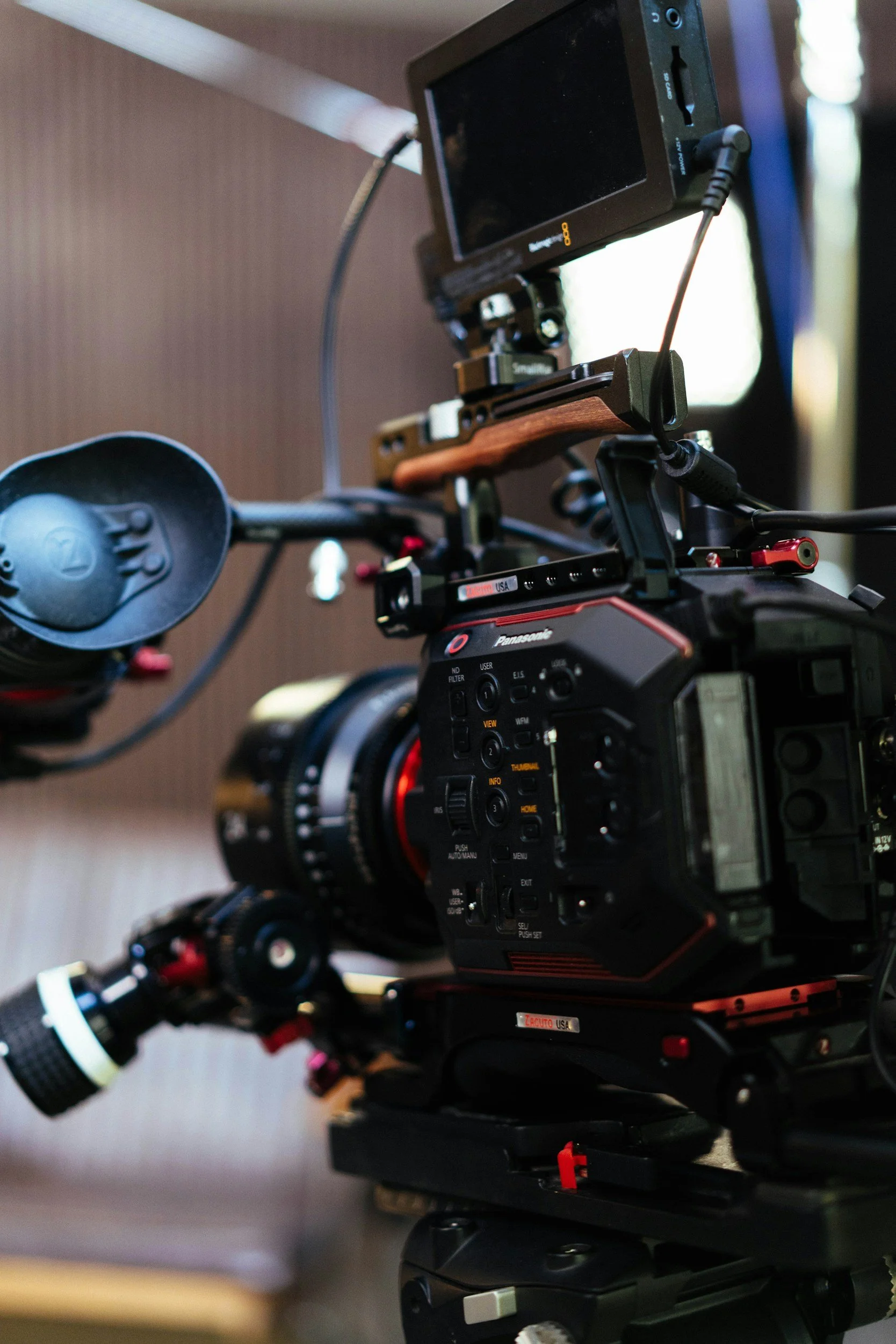 A professional video camera with various controls and attachments, mounted on a tripod, with an external monitor attached.