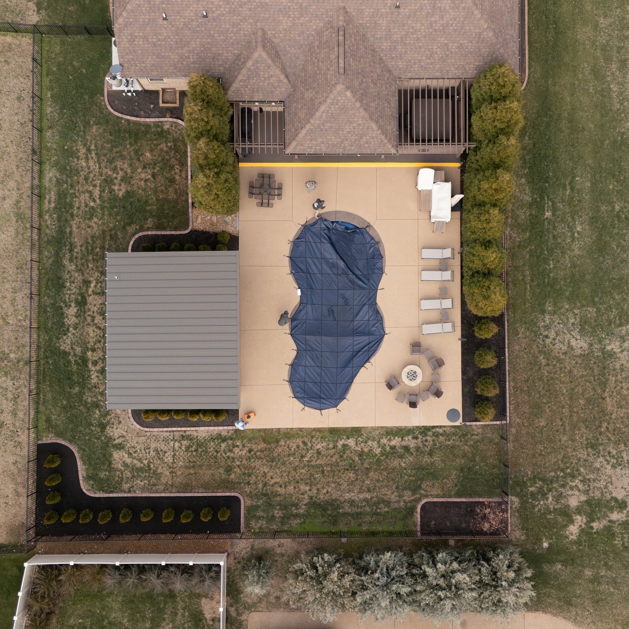 A backyard with a covered swimming pool, lounge chairs, and a fire pit surrounded by outdoor furniture, with a house and landscaped yard.