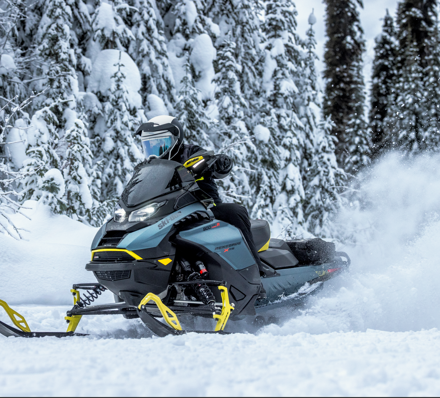 En person kjører snøscooter gjennom snødekt skog, iført hjelm og vinterutstyr.