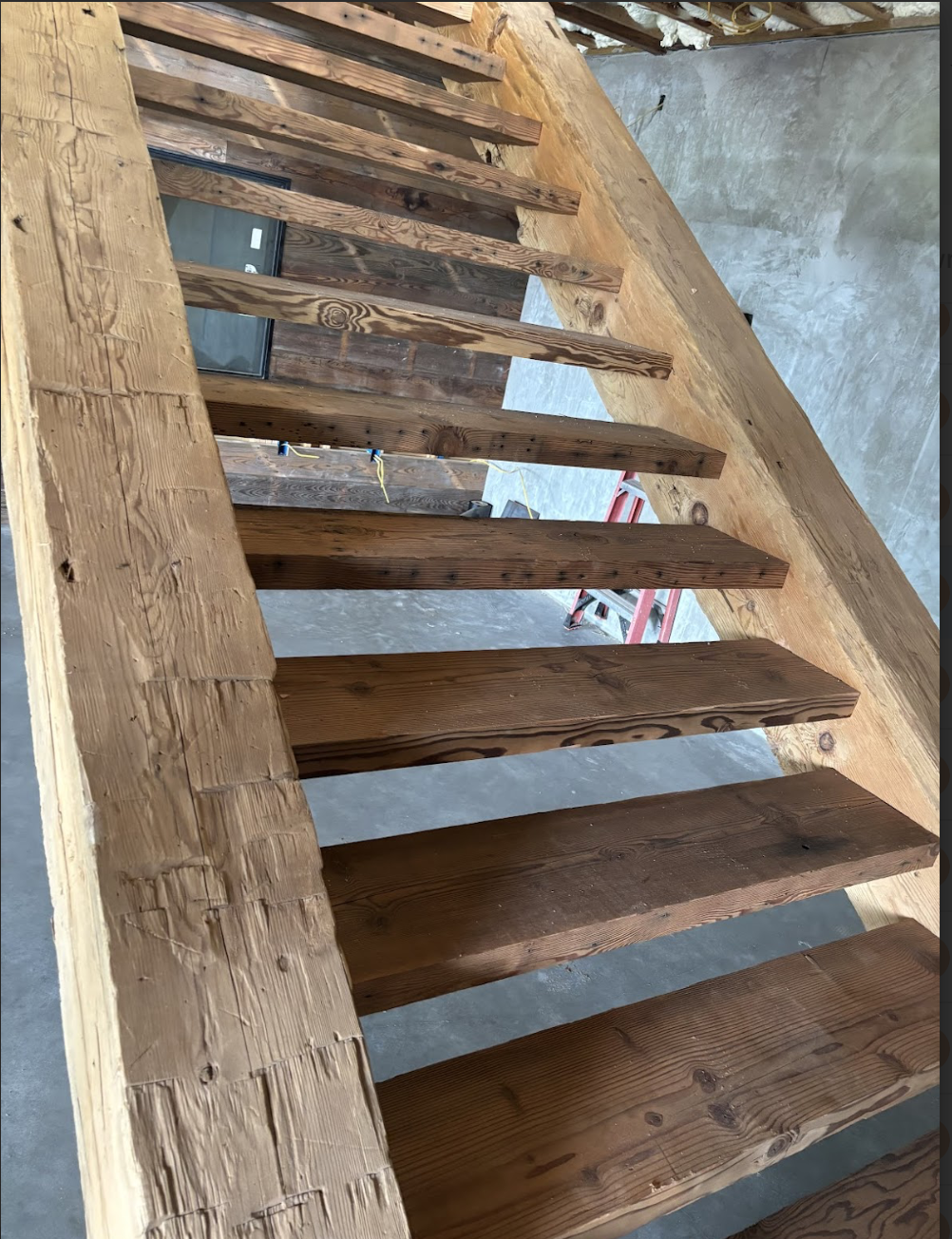 Wooden stairs under construction in a building, with visible wooden beams and an unfinished interior.