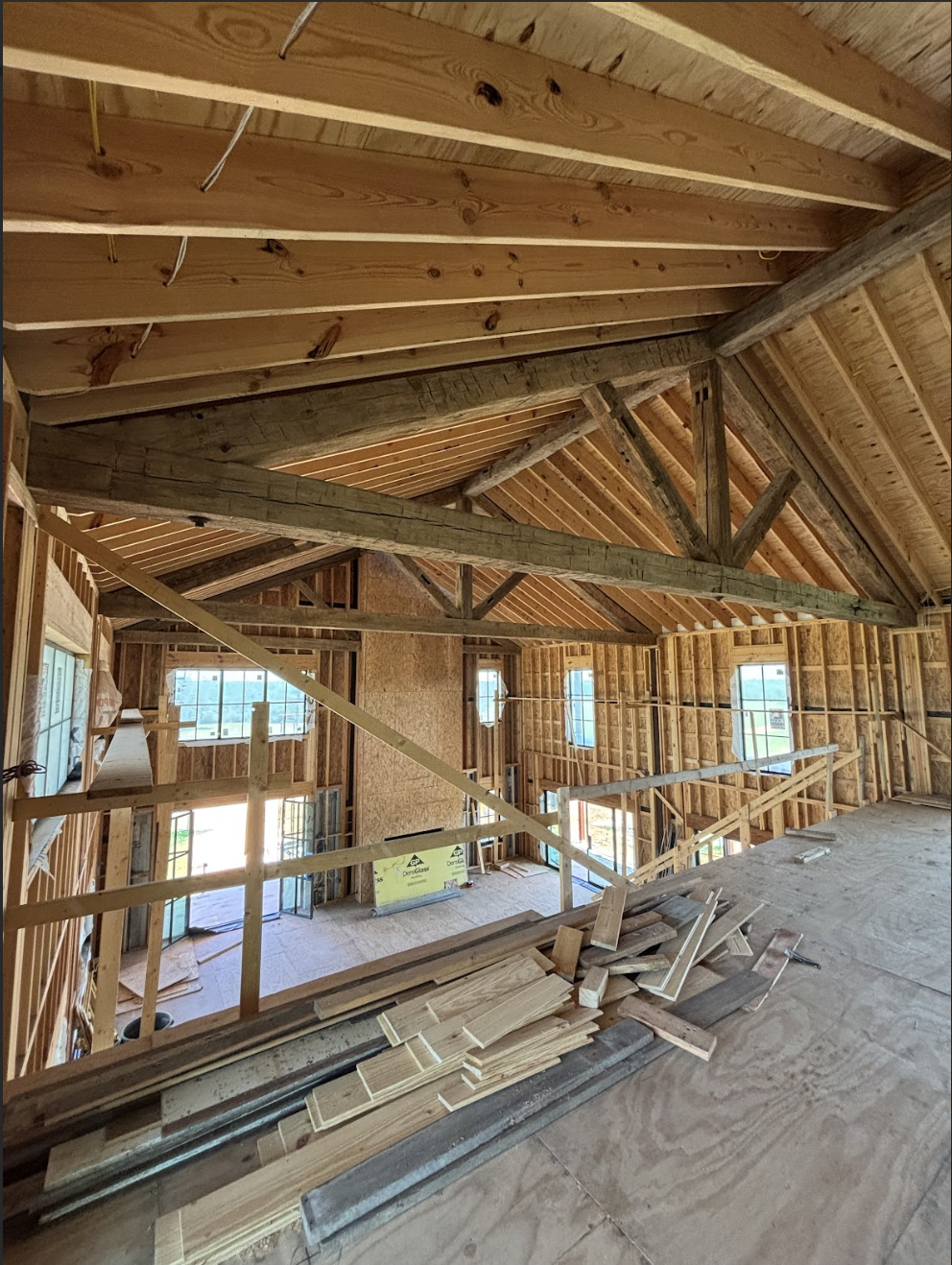 Interior of a house under construction with wooden framing and roofing, construction materials, and scaffolding in place.