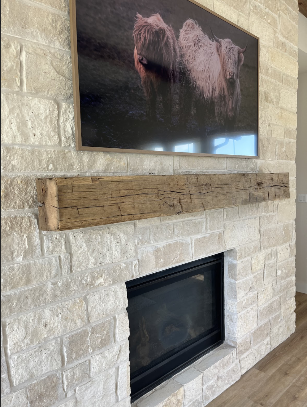Close-up of a stone fireplace with a wooden mantel and a framed picture of two Highland cows hanging above it.