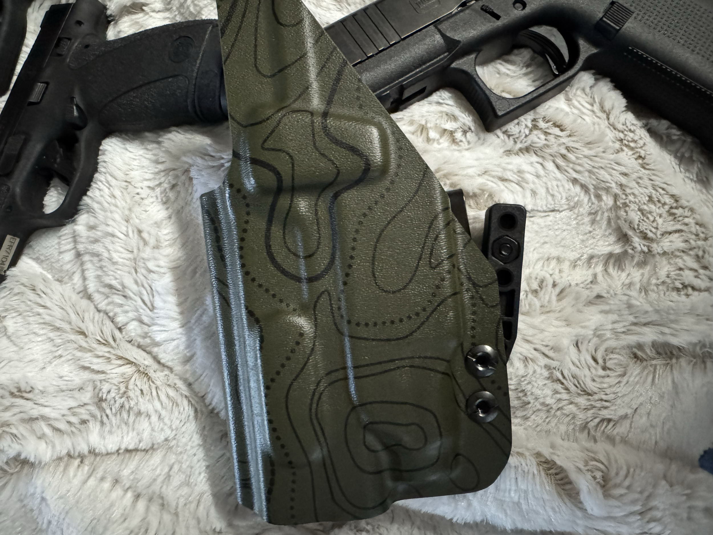 A black handgun with a green fabric sleeve draped over it, placed on a white, fluffy surface.