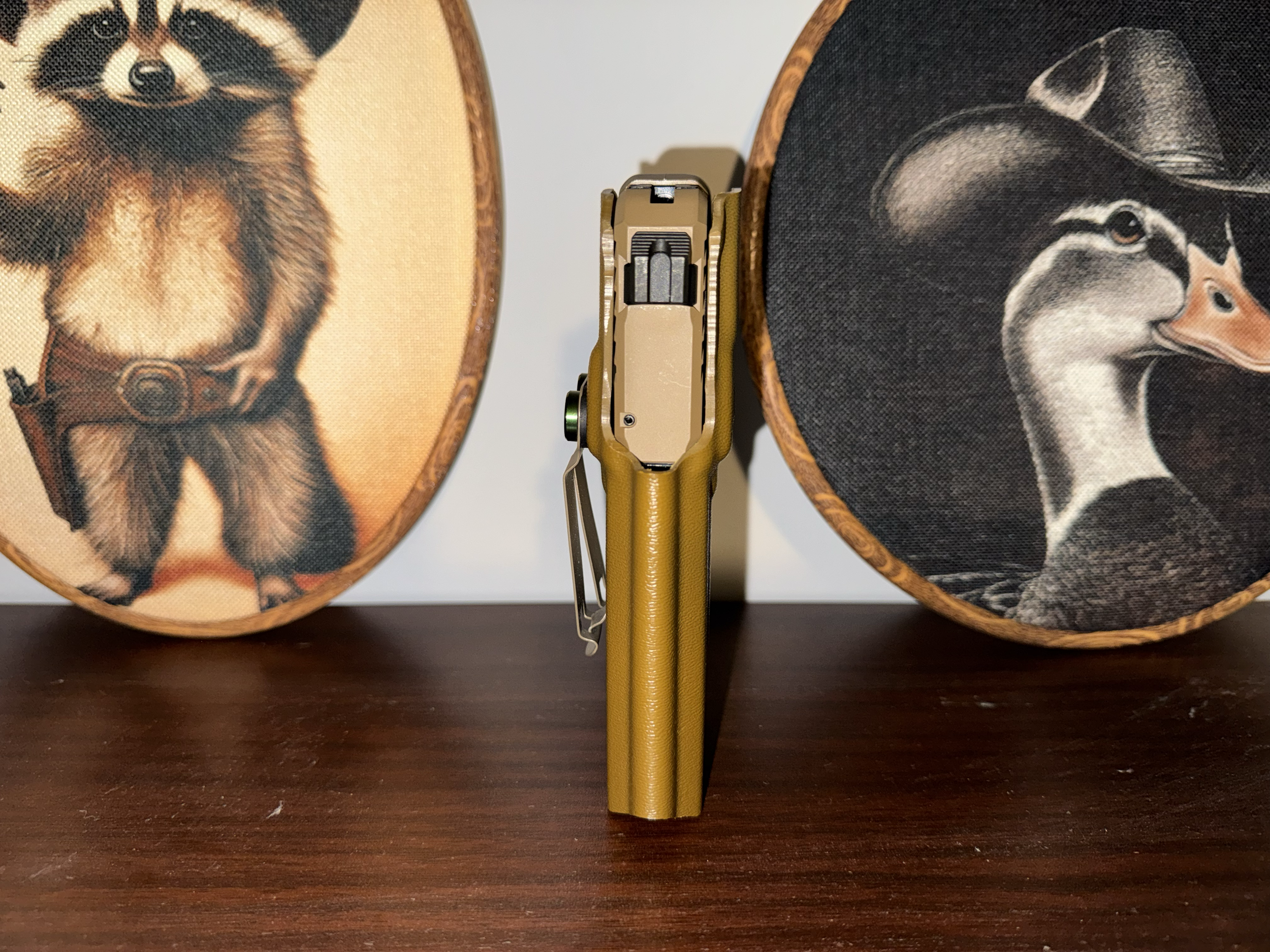 Close-up view of a handgun positioned between two decorative round objects with animal images, one featuring a dog and the other a duck, all on a dark wooden surface.