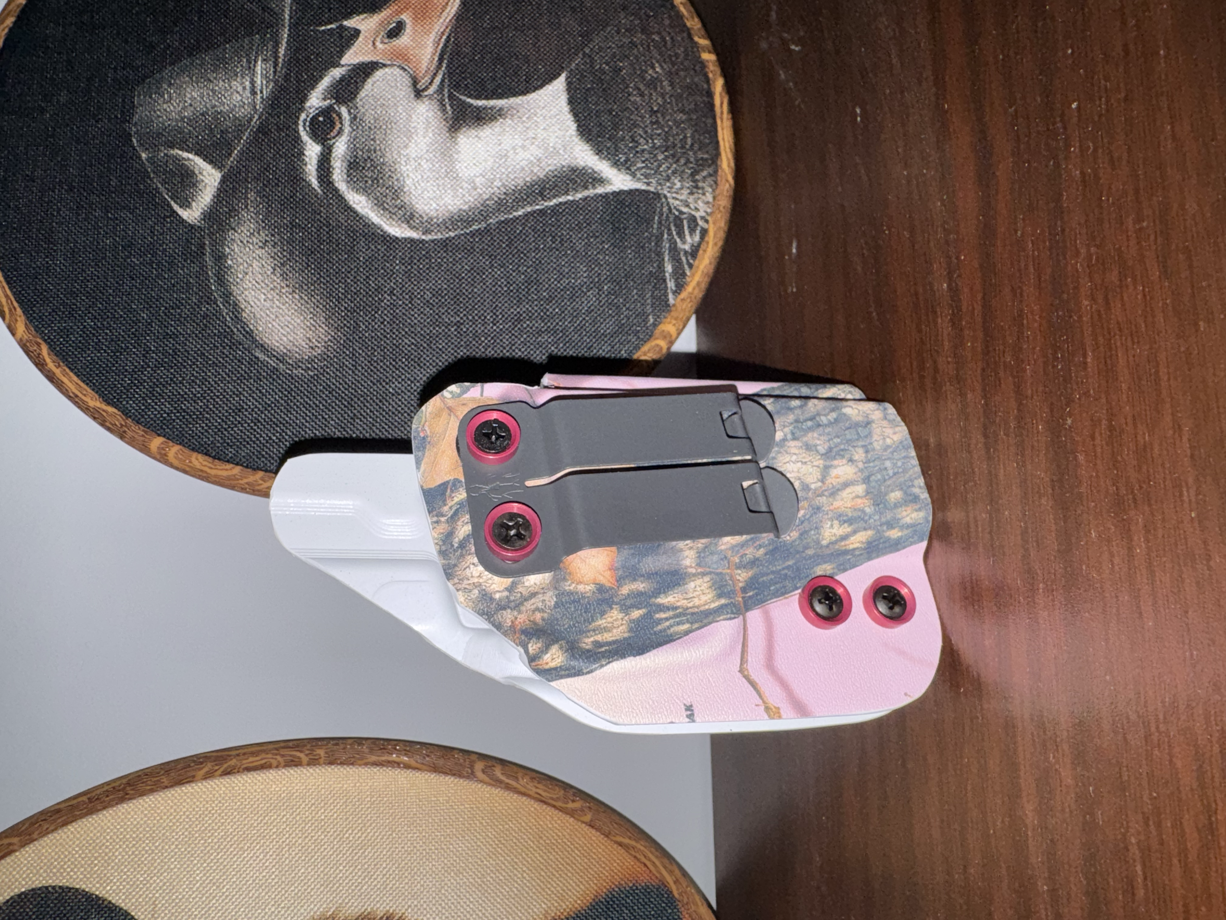 Close-up of a decorative table with a wooden surface, a round cloth featuring a horse illustration, and objects including a remote control with pink accents and pink and black screws.