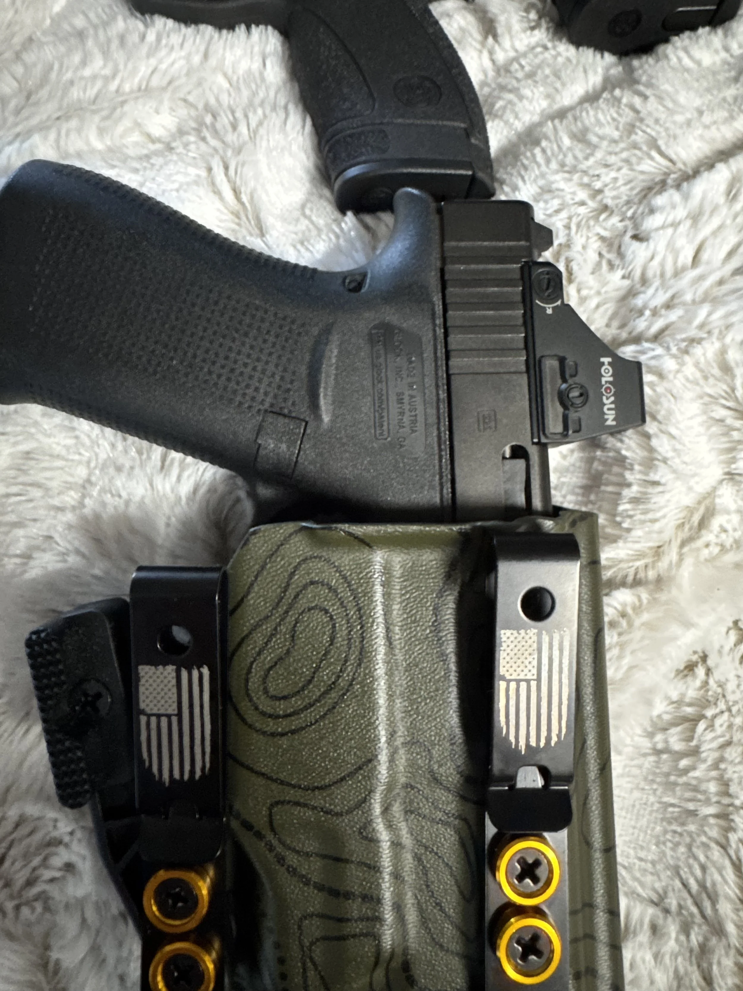Close-up of a handgun with a green grip, gunmetal gray slide, and yellow accents, resting on a white, fluffy surface.