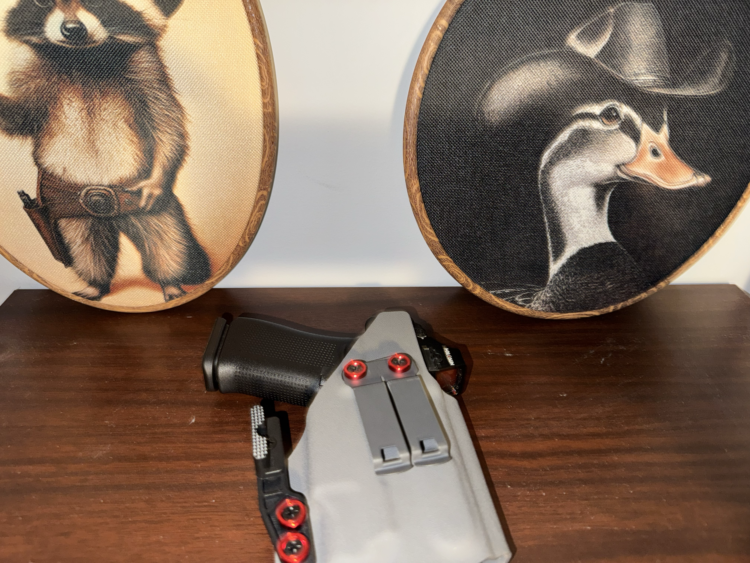 Close-up of a firearm with a gray and black body resting on a wooden surface, with a device attached to the barrel, and two boxes featuring dog artwork behind it.