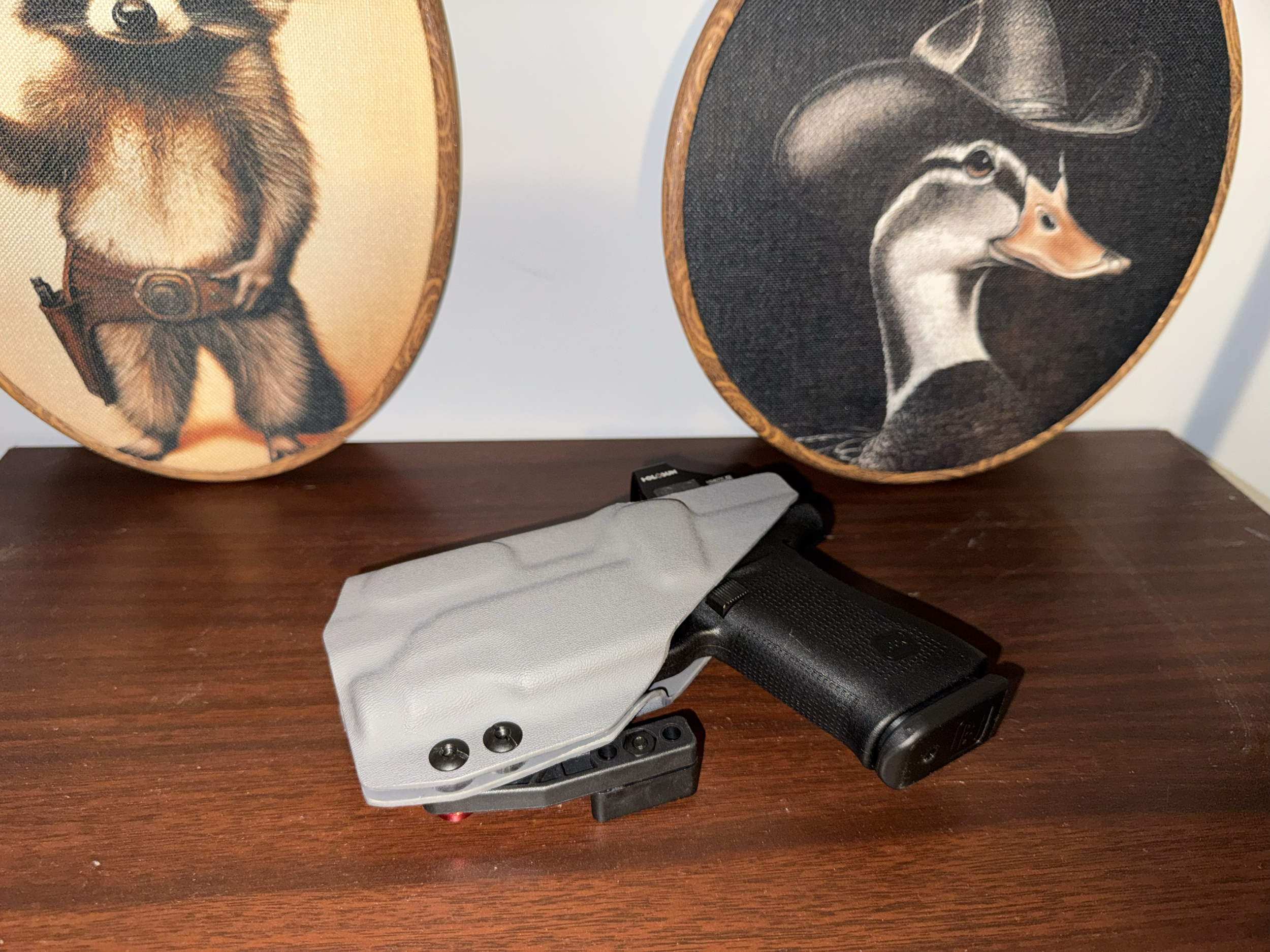 Two decorative round panels featuring animal portraits, one of a dog and one of a duck, placed on a wooden surface. In front of the panels are a gray cloth, a black flashlight, and a black scope.
