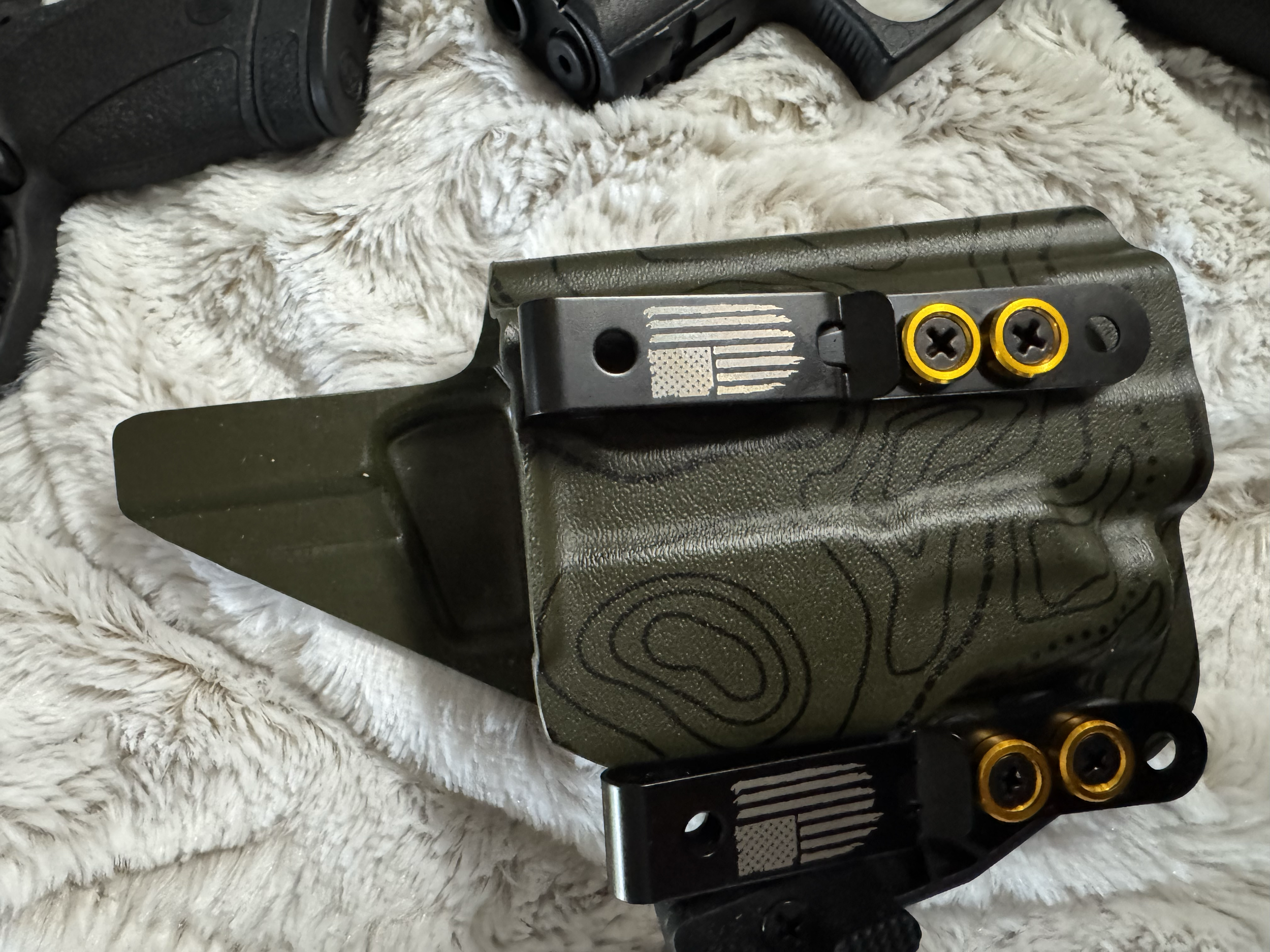 Close-up of firearm parts on a fluffy white surface, showing the slide with an American flag engraving and yellow screw accents.