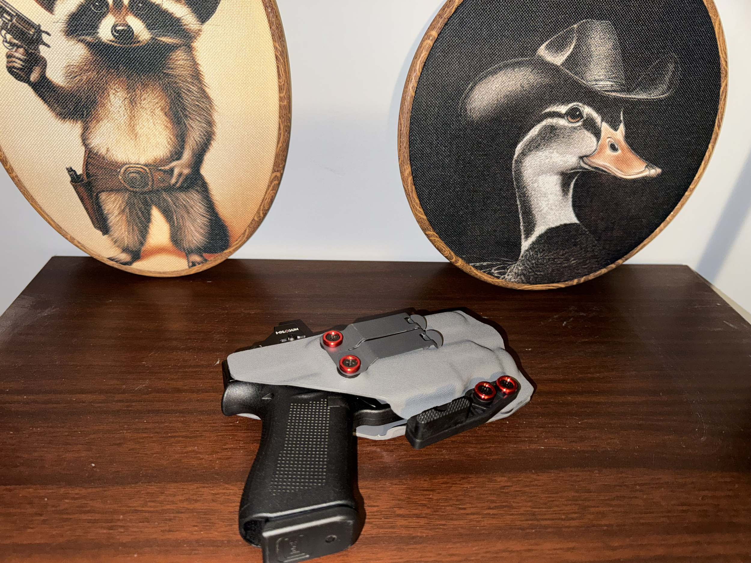 Two embroidered art pieces featuring a dog and a wolf, mounted on wooden frames, placed on a wooden surface with a toy gun in front.