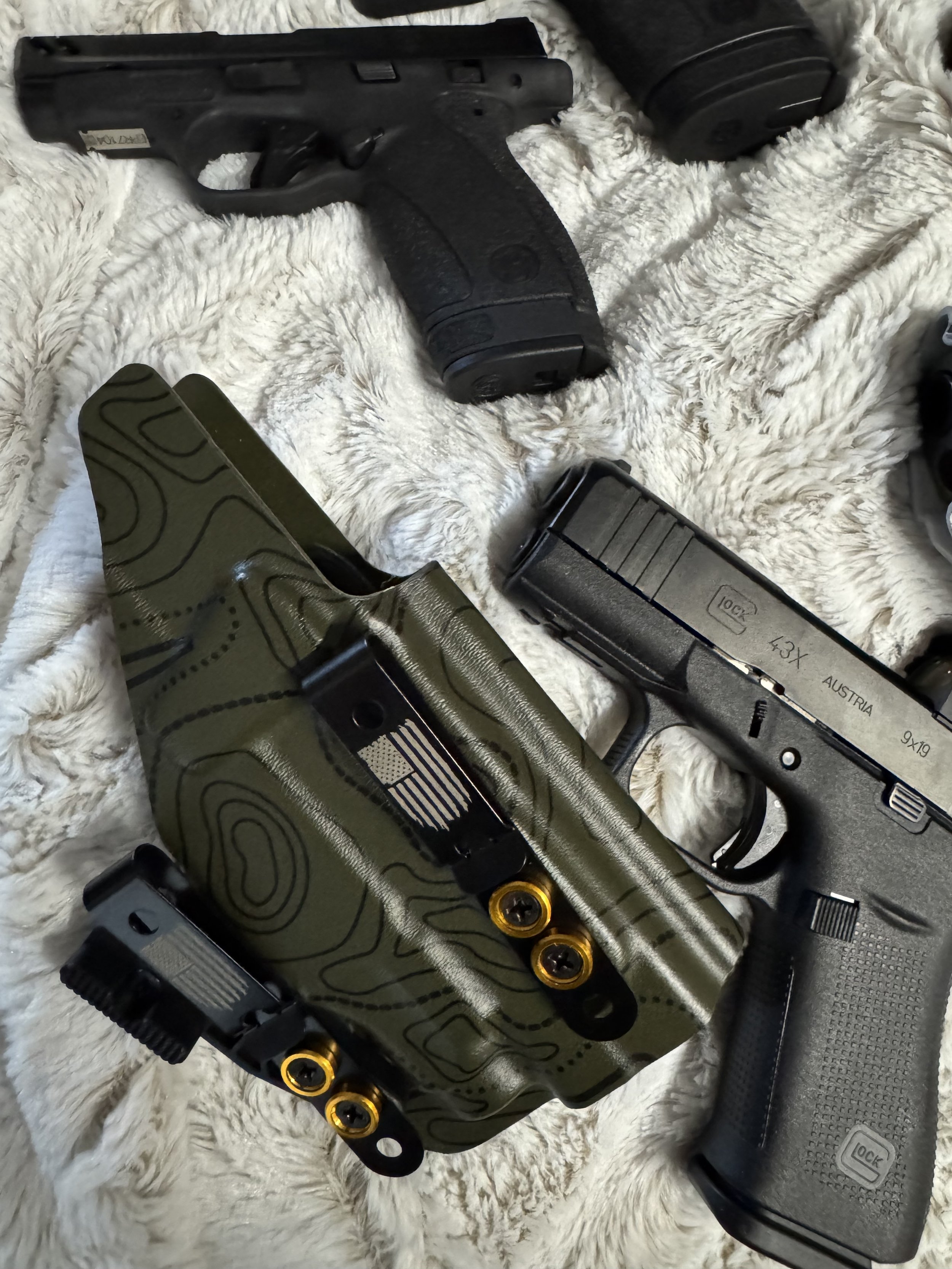 Several handguns and magazines placed on a soft, fluffy white surface.
