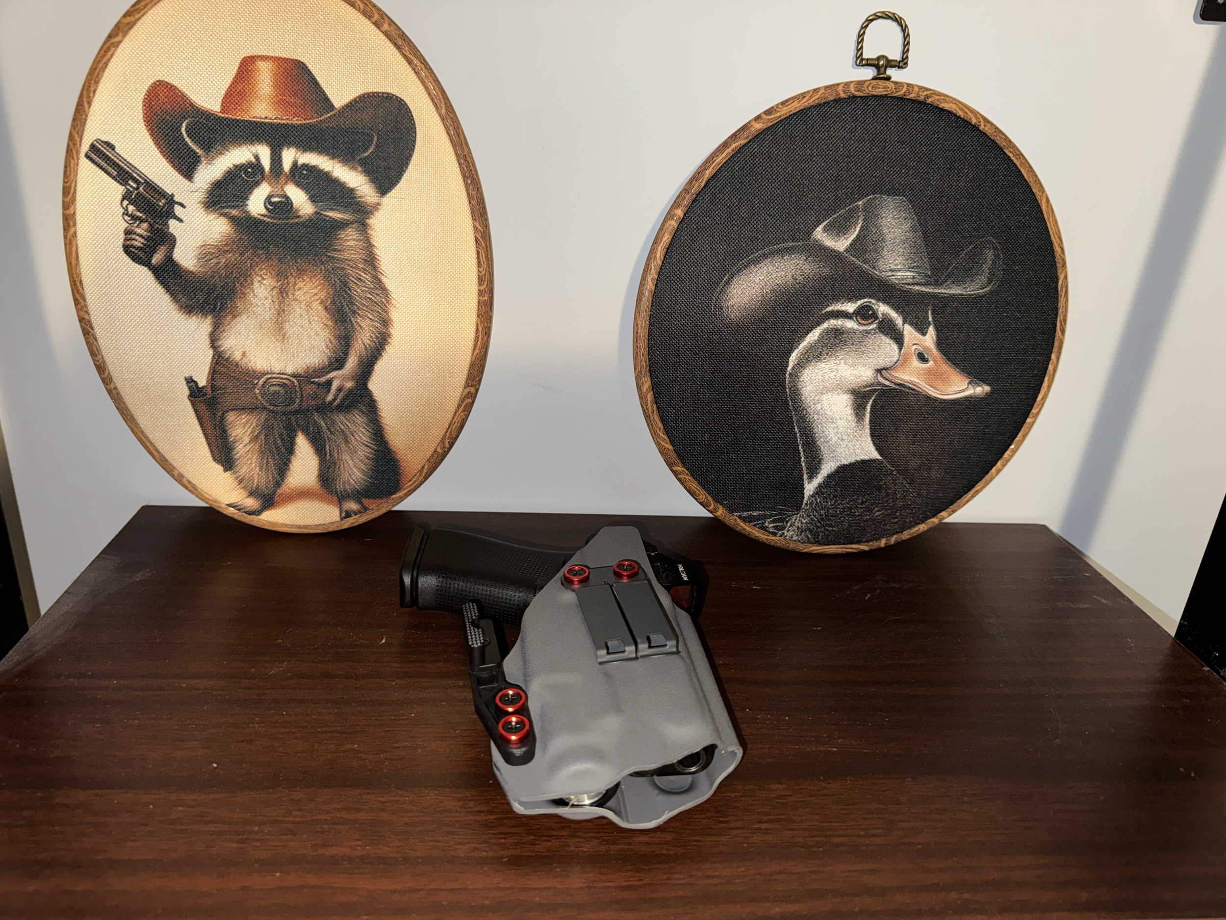 Two decorative oval wall hangings with animal illustrations, a small black device with red buttons, and a video game controller with a gray and black design on a wooden surface.