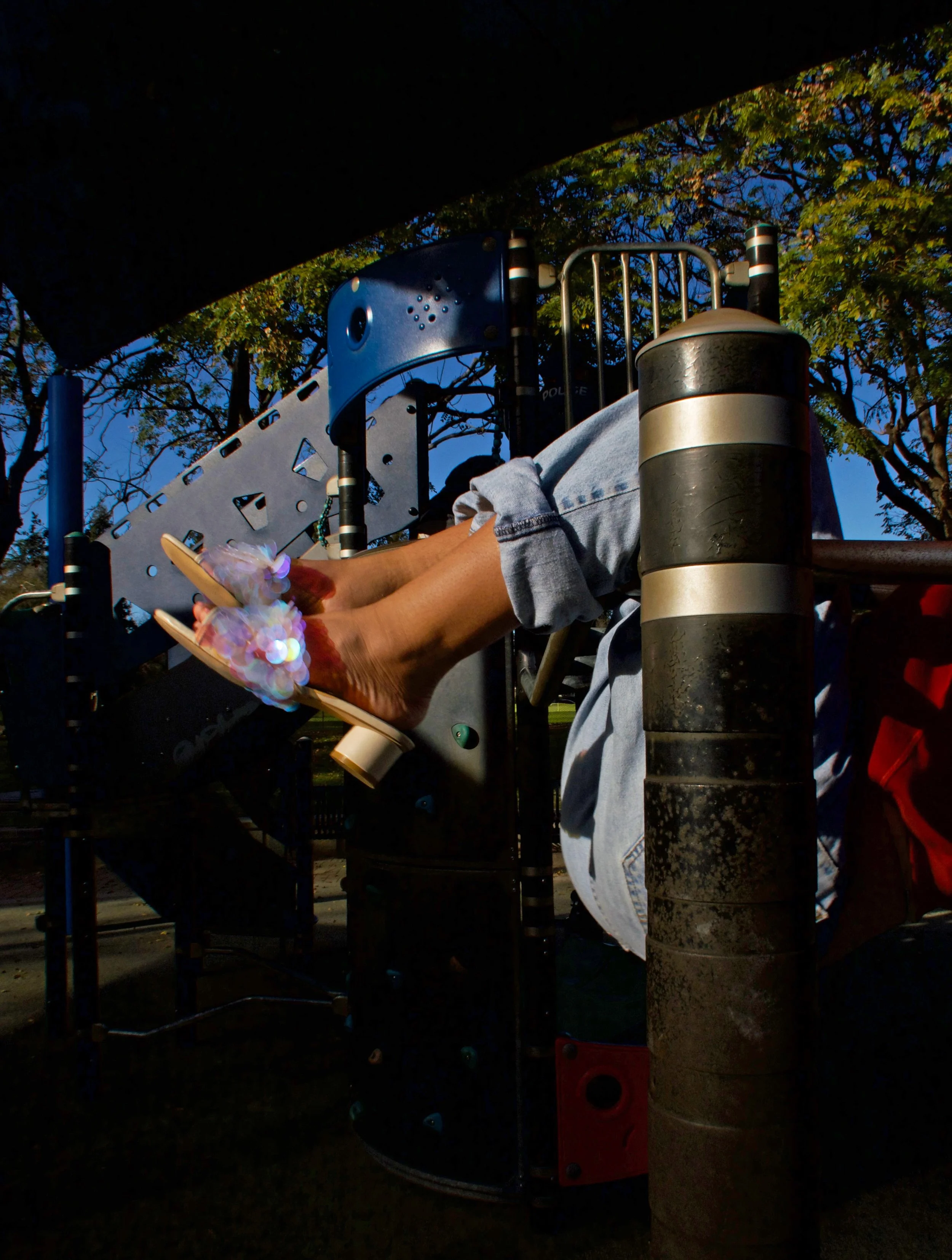 Person's feet in colorful high-heeled sandals resting on playground equipment.