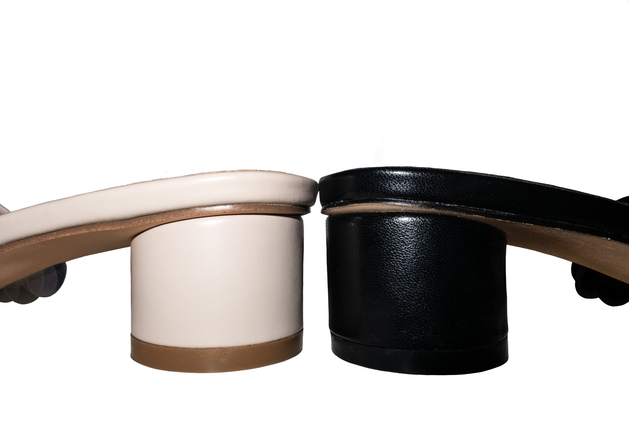 Close-up of two pairs of high-heeled shoes with chunky heels; one in white with a brown sole and heel, and the other in black with a similar sole and heel.