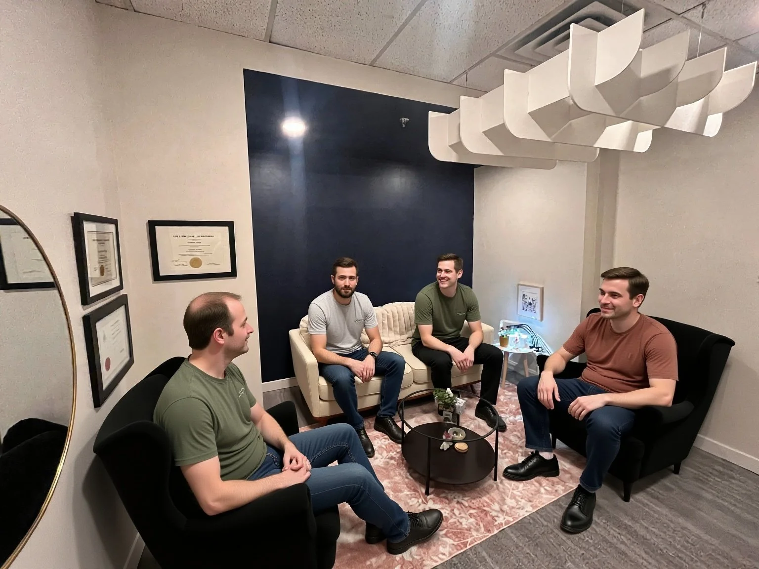 Four men sitting in a modern therapy room, engaged in conversation, with certificates on the wall and a decorative ceiling baffle above.