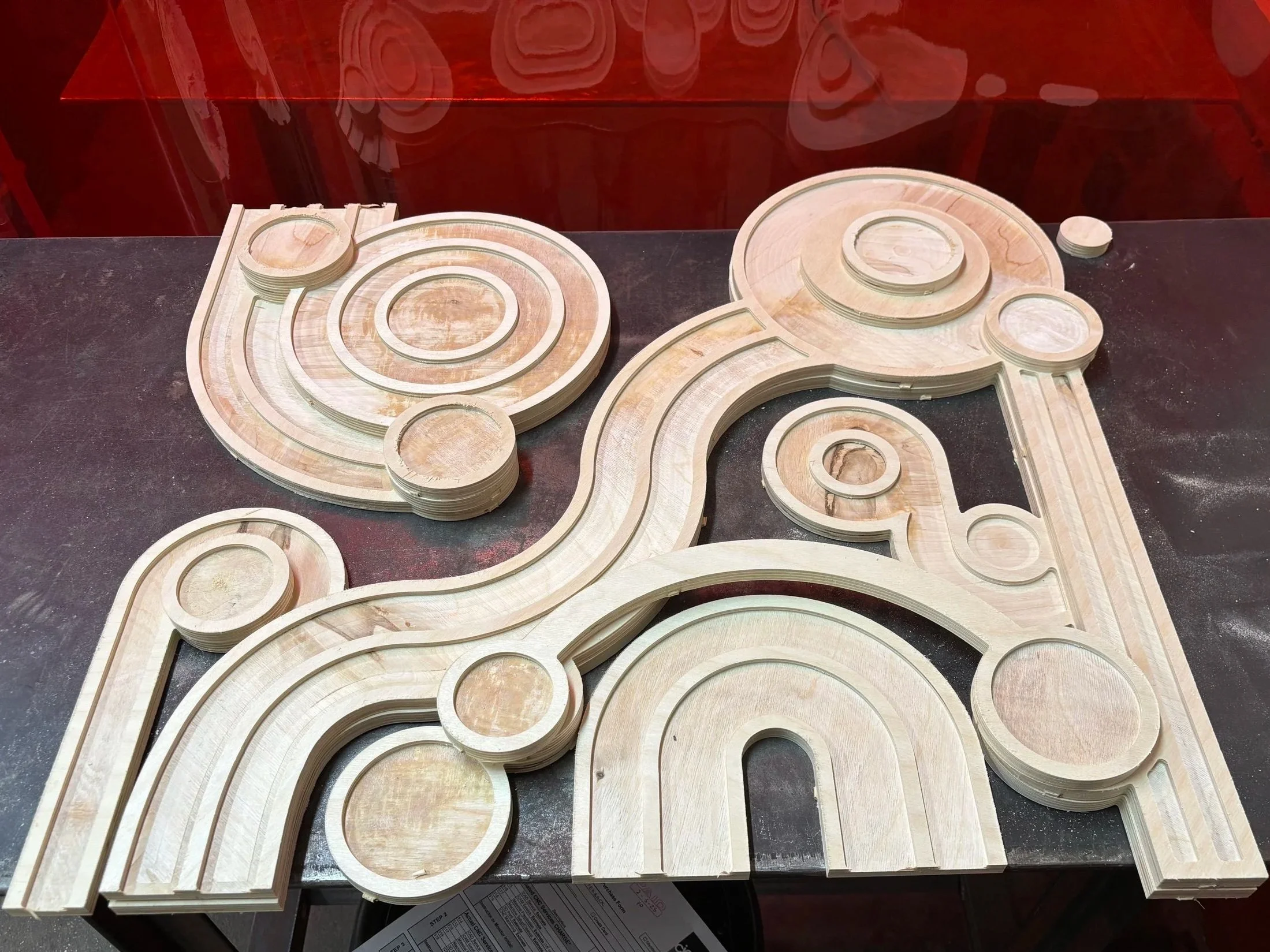 Unassembled wooden puzzle with circular and curved pieces arranged on a dark surface.