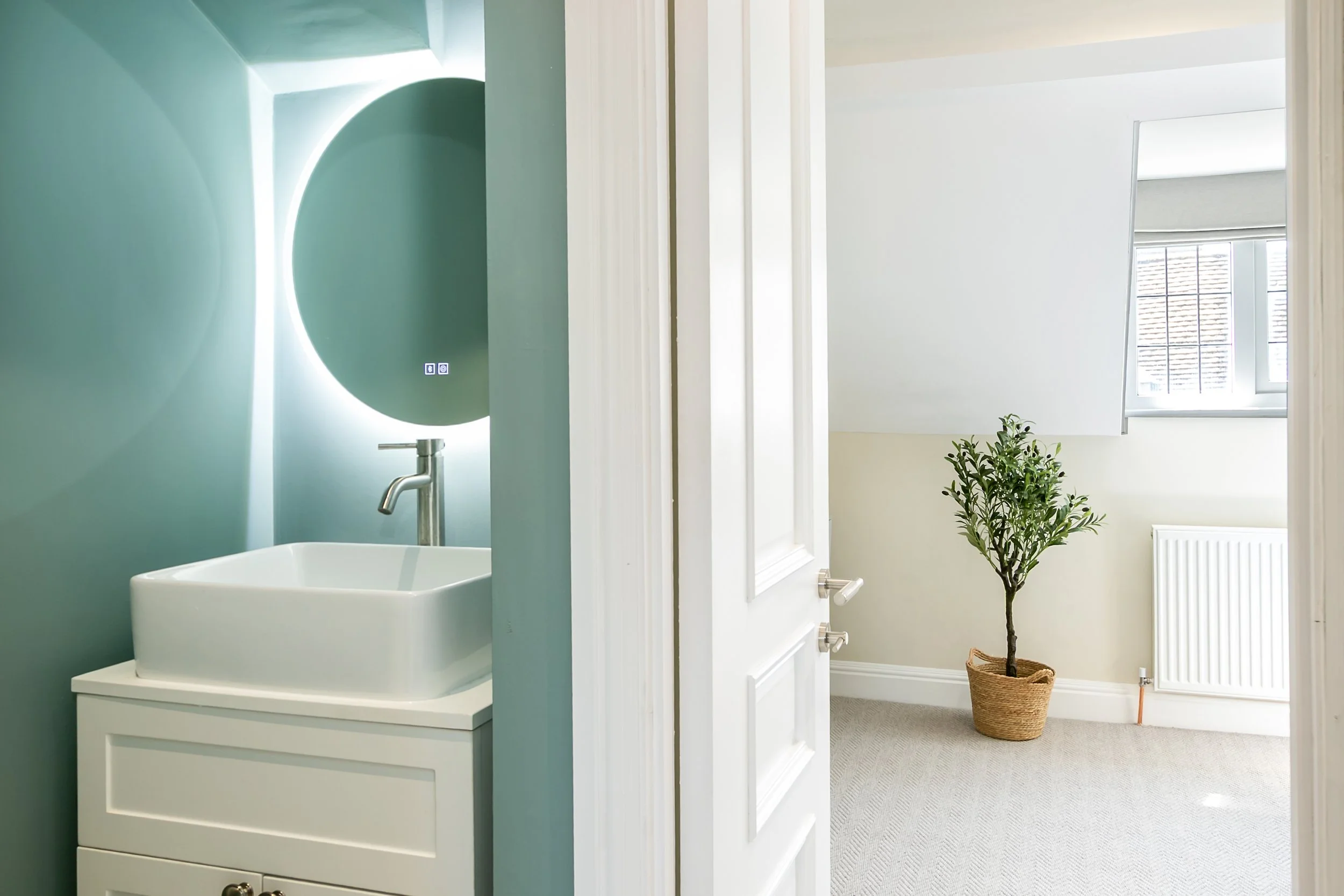 Partially open white door revealing a room with a potted plant, window, radiator, and white wall.