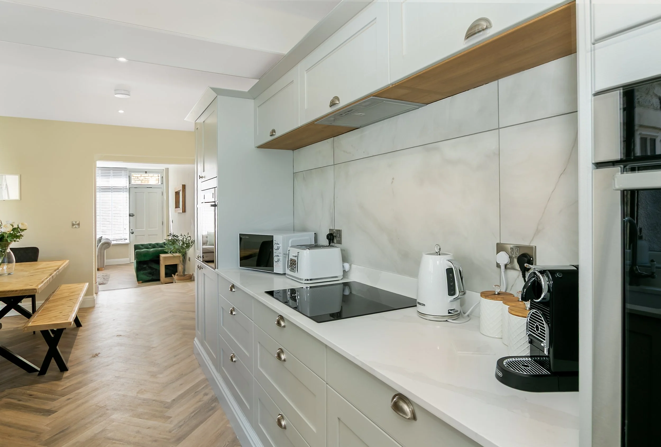 Modern kitchen with white cabinets, marble backsplash, and black countertop appliances in an open-plan living space.