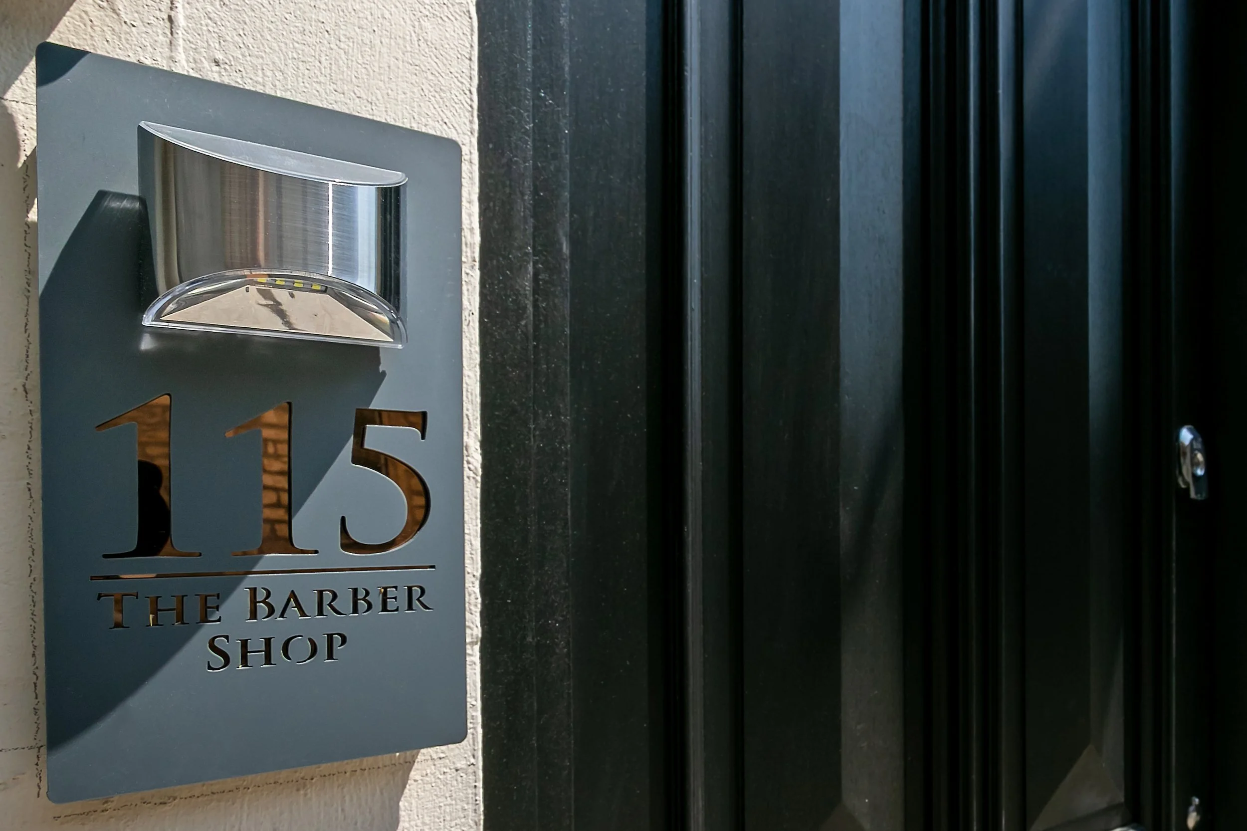House number 115 and a sign reading 'The Barber Shop' on a wall near a black door.