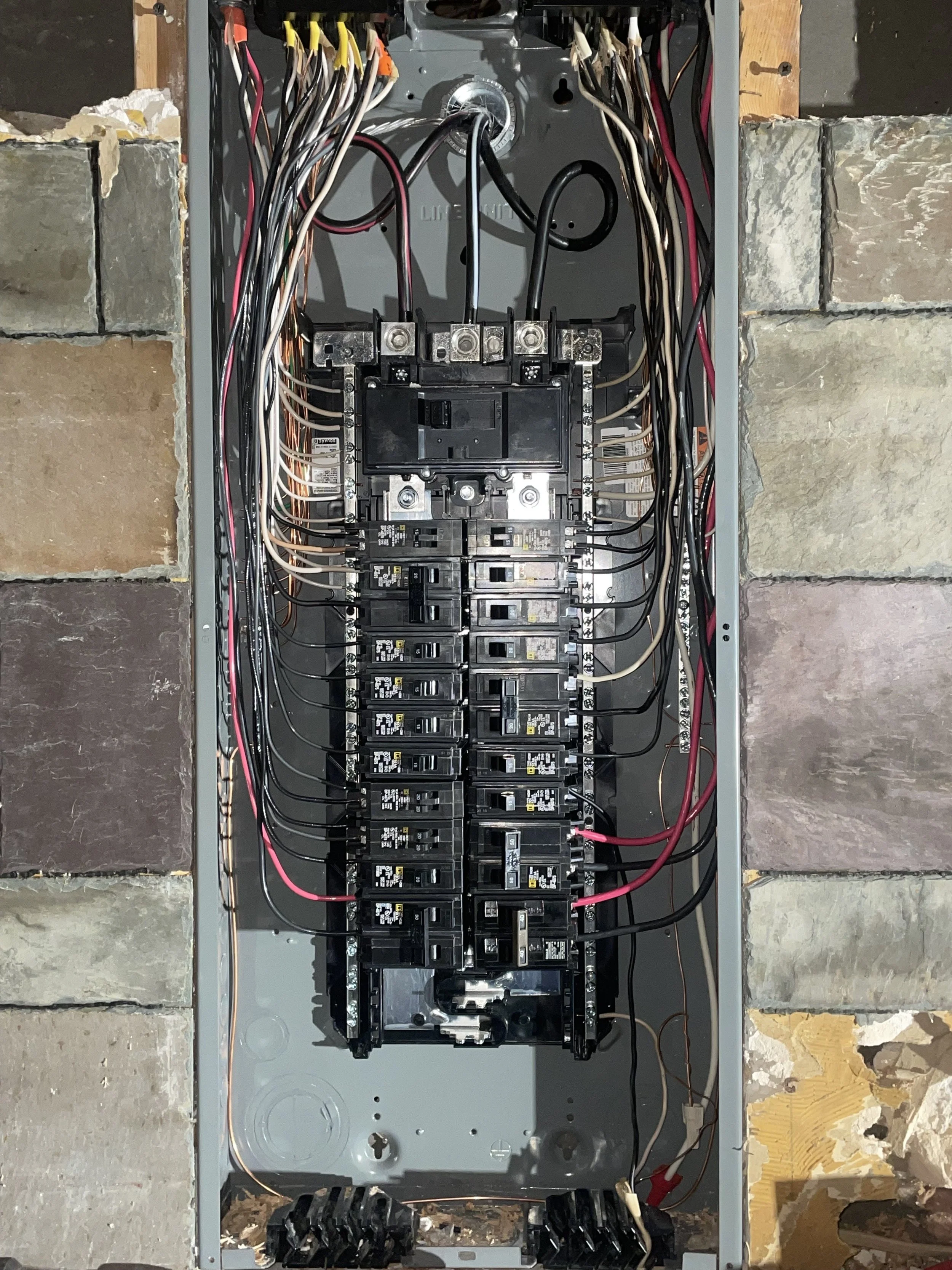 Open electrical panel with circuit breakers and wiring inside a wall cavity.