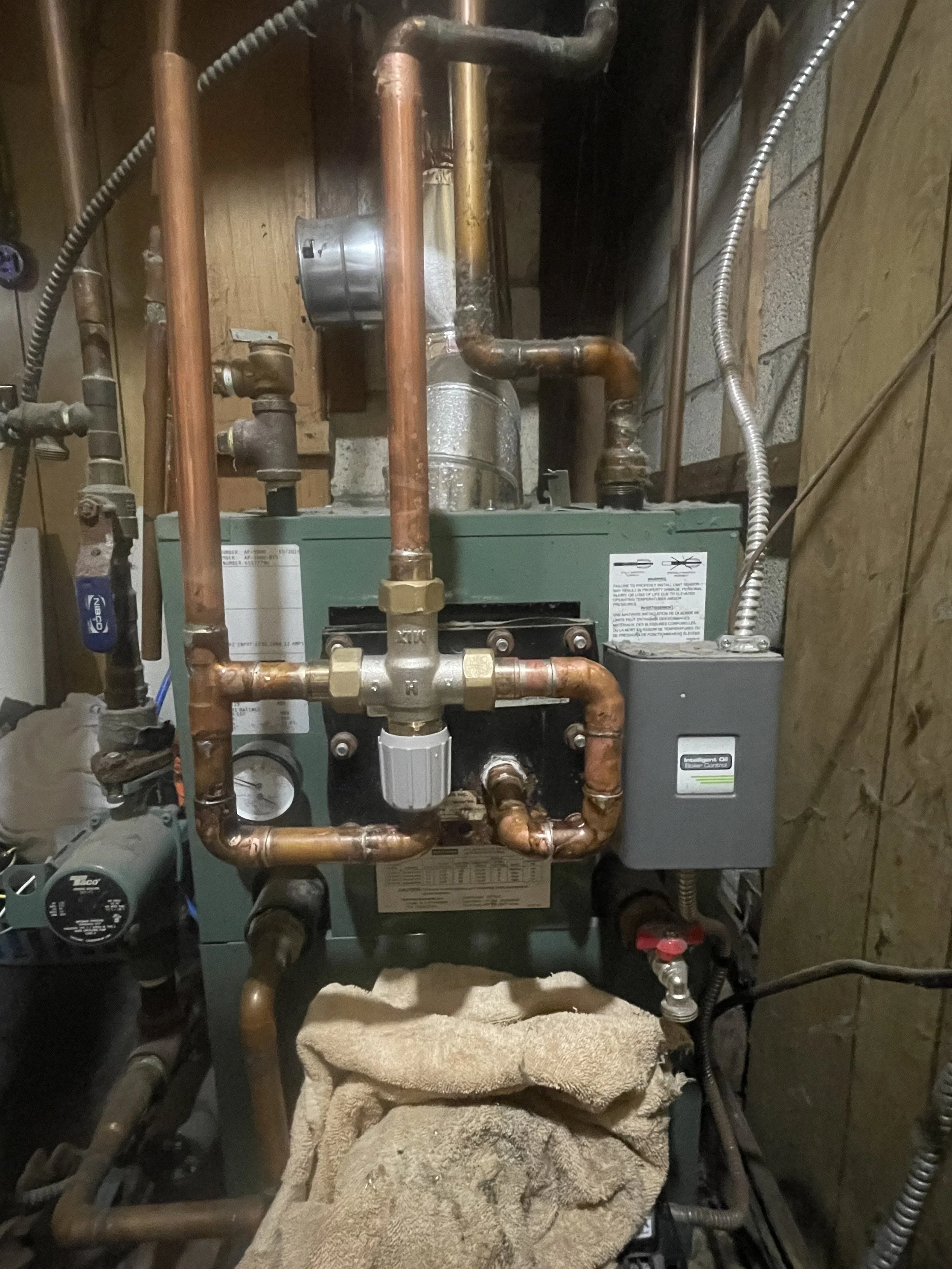 A residential HVAC furnace with copper piping, electrical connections, and a towel draped over the bottom.