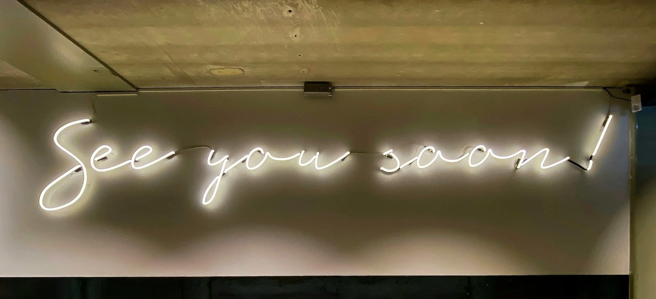 Neon sign with the message 'see you soon!' written in cursive script, glowing white.