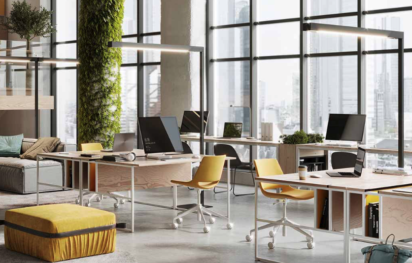 Modern open-plan office space with large windows, multiple desks with computers and chairs, a couch, a green wall, and a city view in the background.