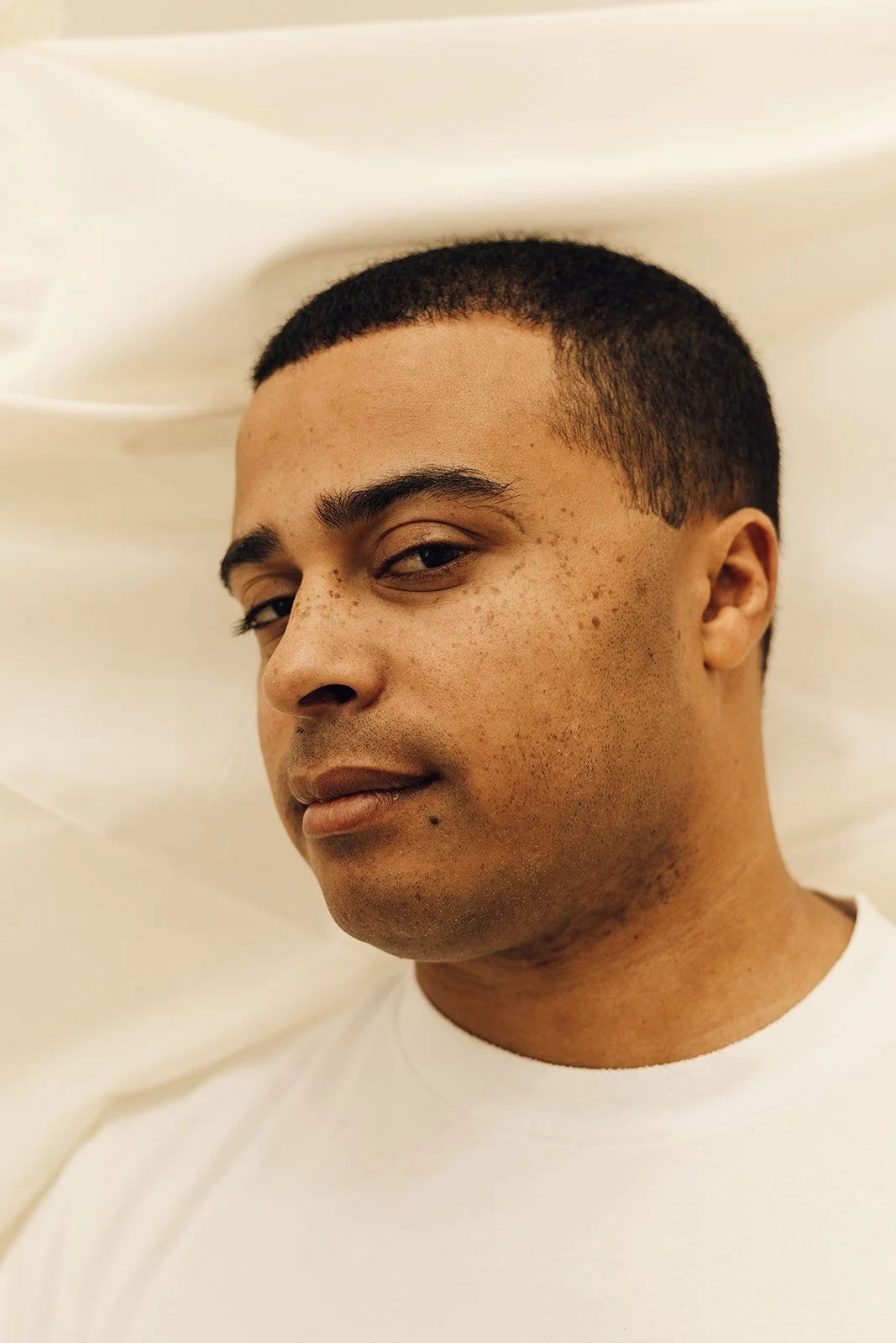 Close-up of a young man with short hair, looking at the camera with a slight smile, against a light background.