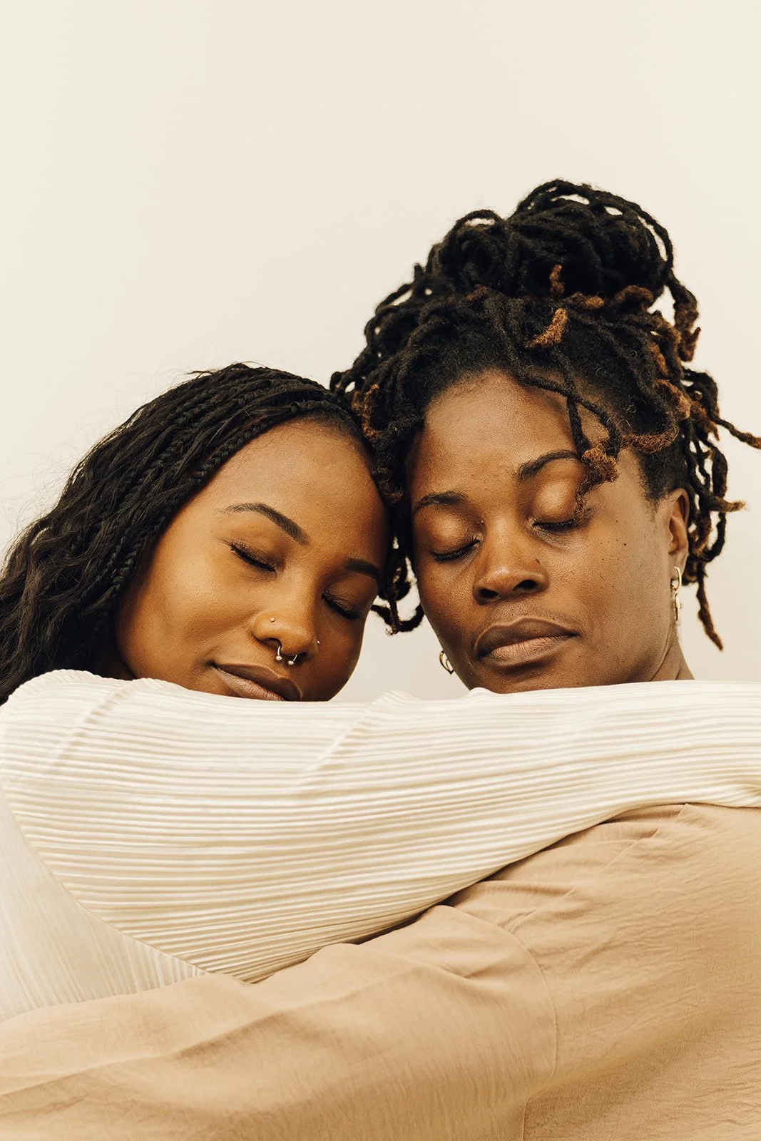 Two women hugging with their eyes closed, sharing an emotional moment, against a plain white background.