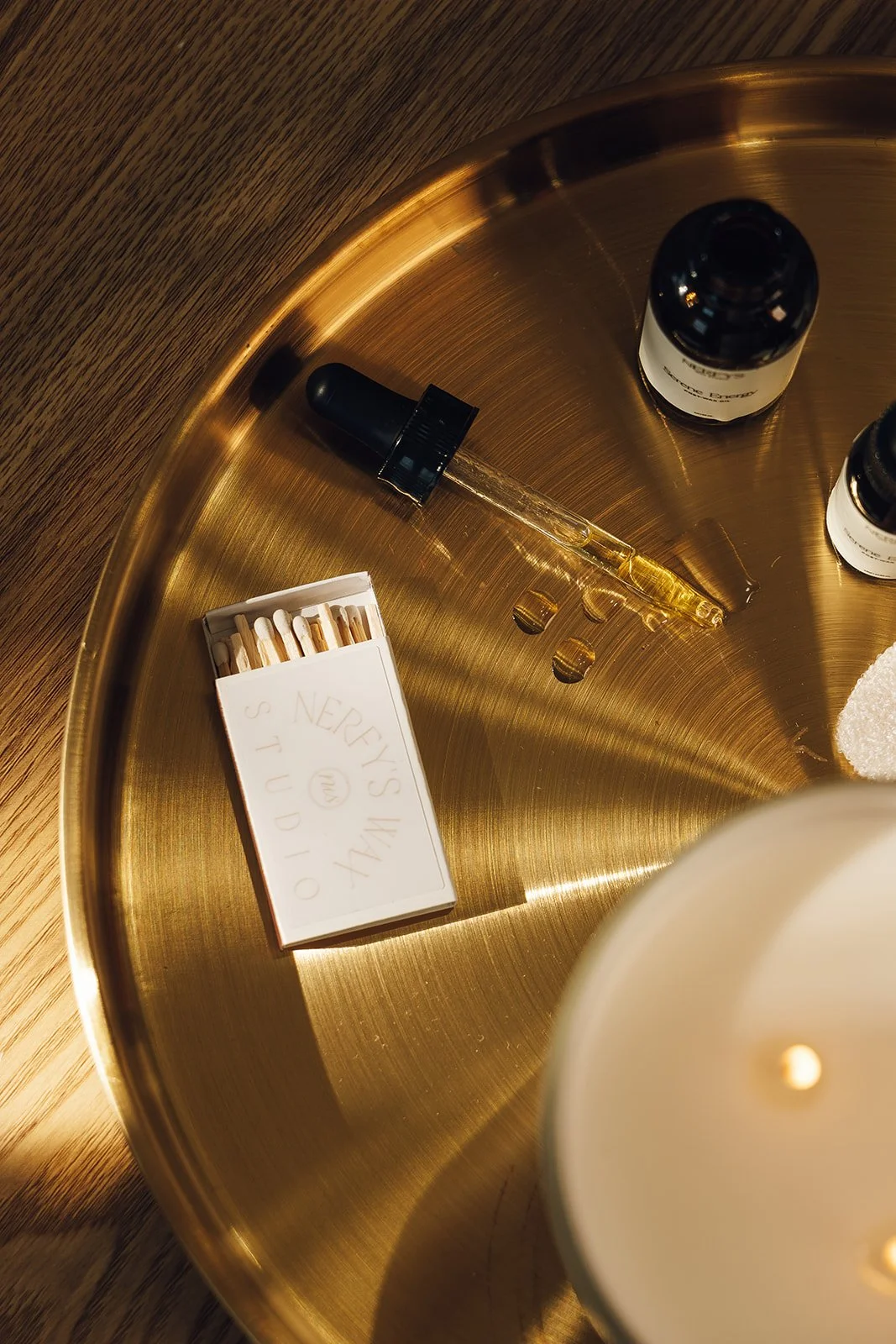 A gold circular tray with essential oils, a small dropper, a box of matches, and a candle in the foreground.