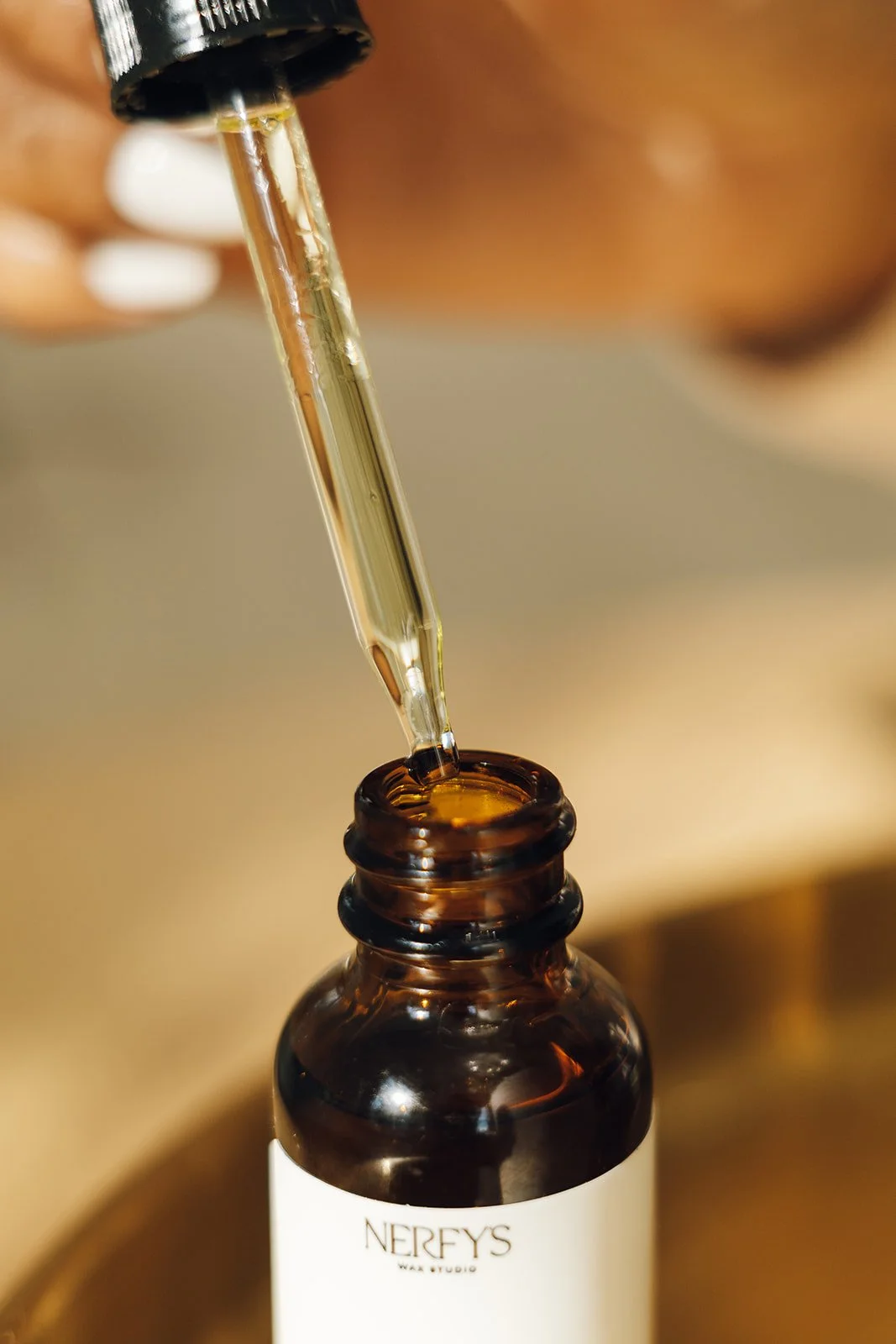Close-up of a brown glass bottle with a dropper, applying Serene Energy Oil. The bottle has a white label with the word 'NERFYS' on it.