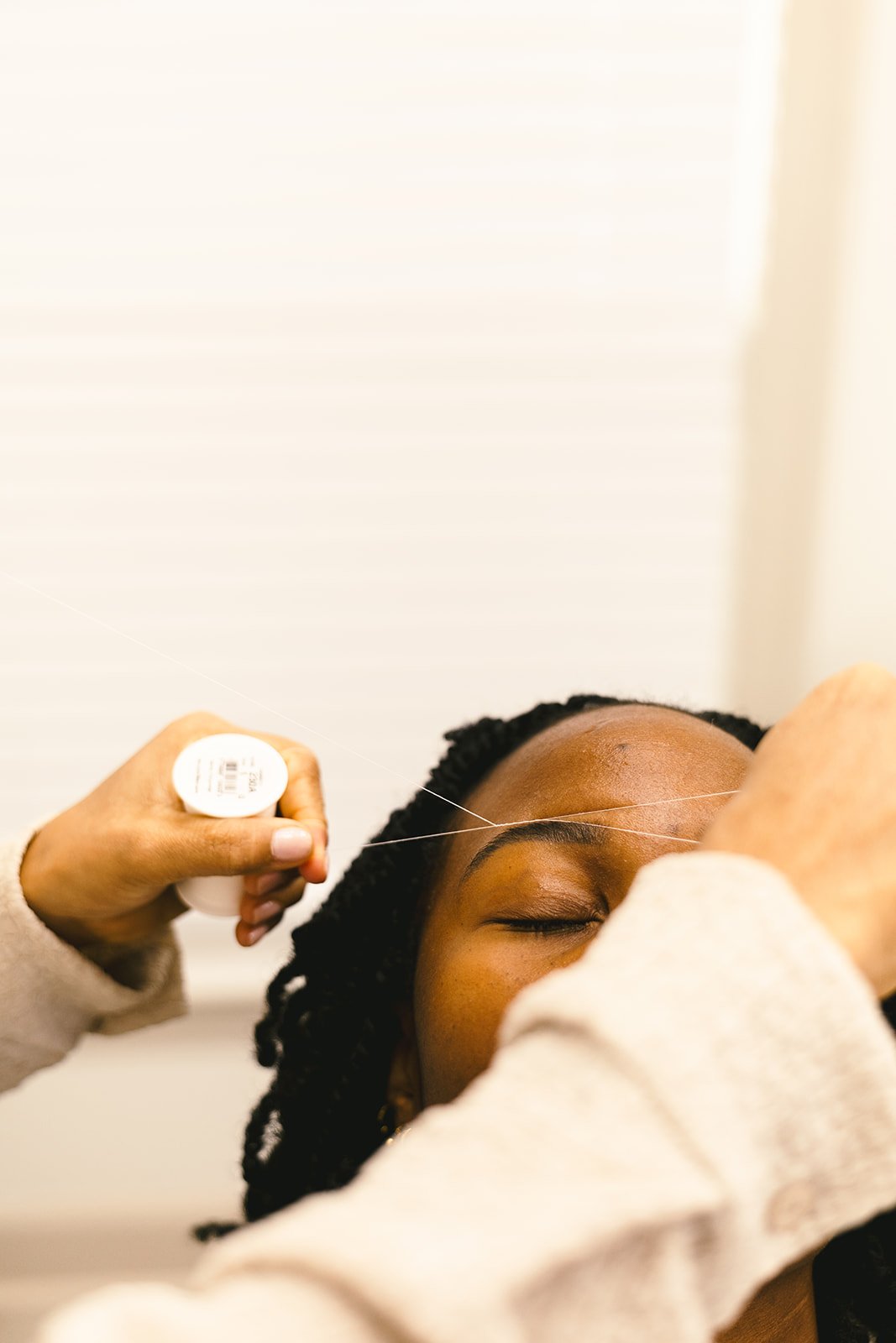 A woman receiving an eyebrow threading service, with her eyes closed.