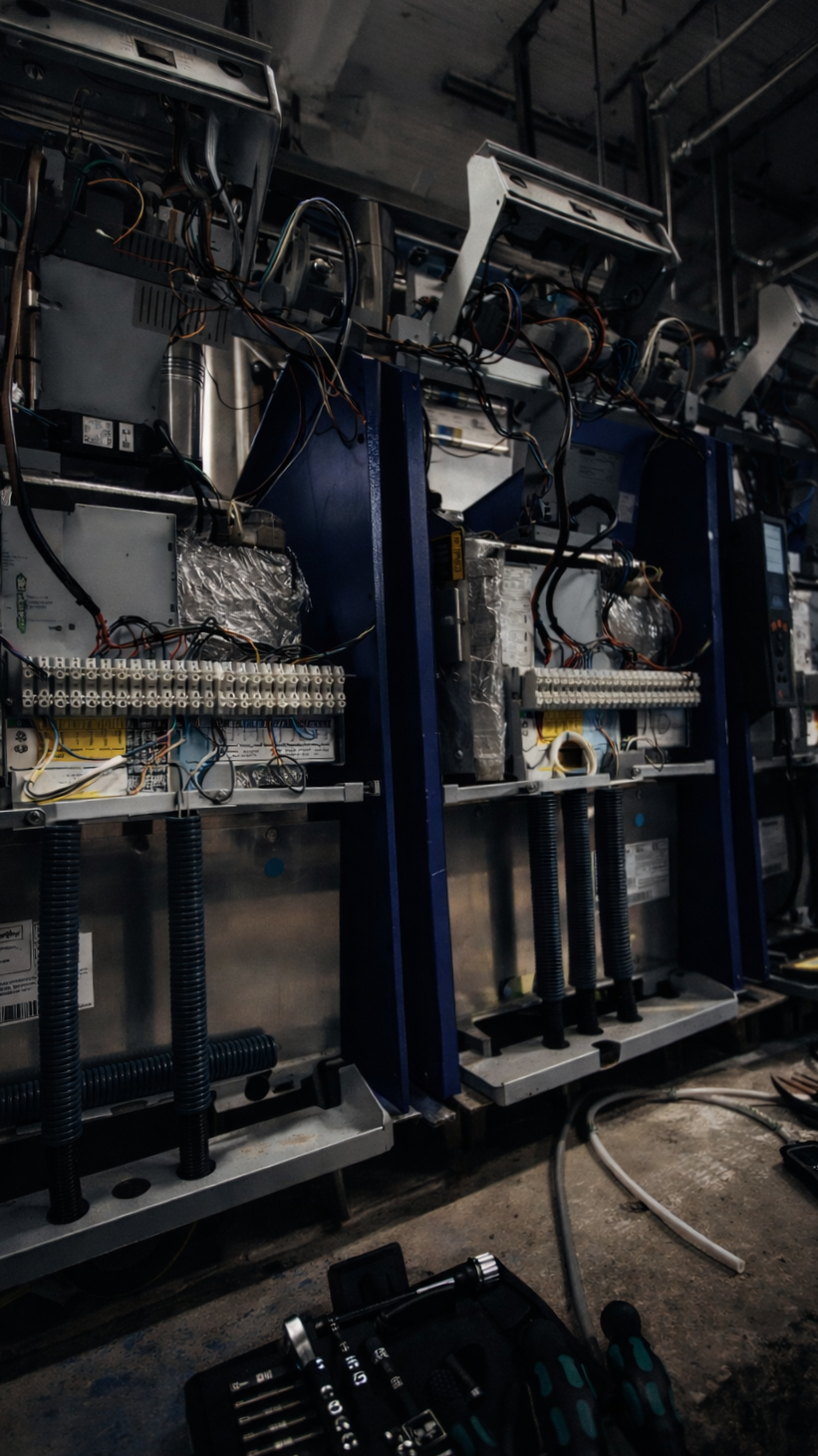 Industrial or commercial electrical equipment or machinery being worked on or assembled, with wires, circuit boards, and tools visible.