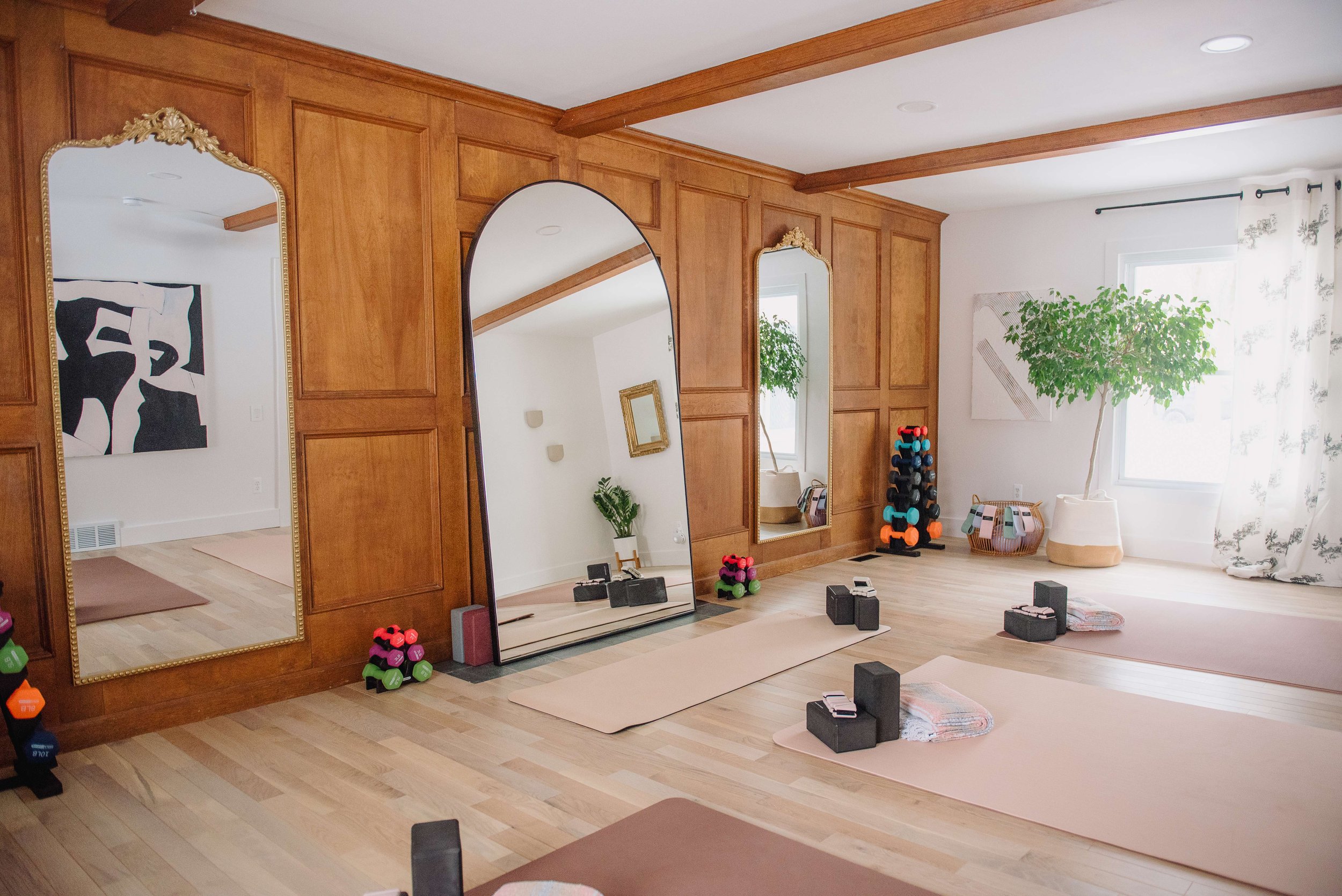 Fitness studio with wooden wall panels, large mirrors, yoga mats, and exercise equipment, including dumbbells and resistance bands.