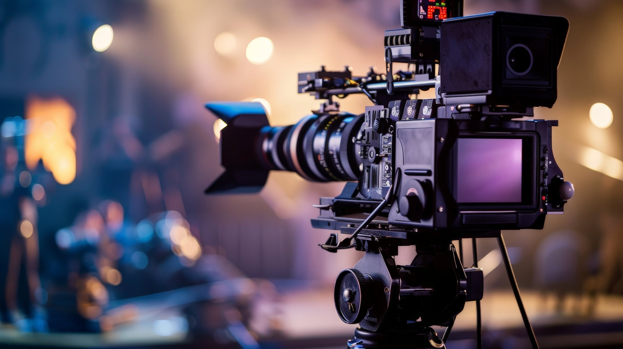 Professional video camera mounted on a tripod with a blurred background of bokeh lights.