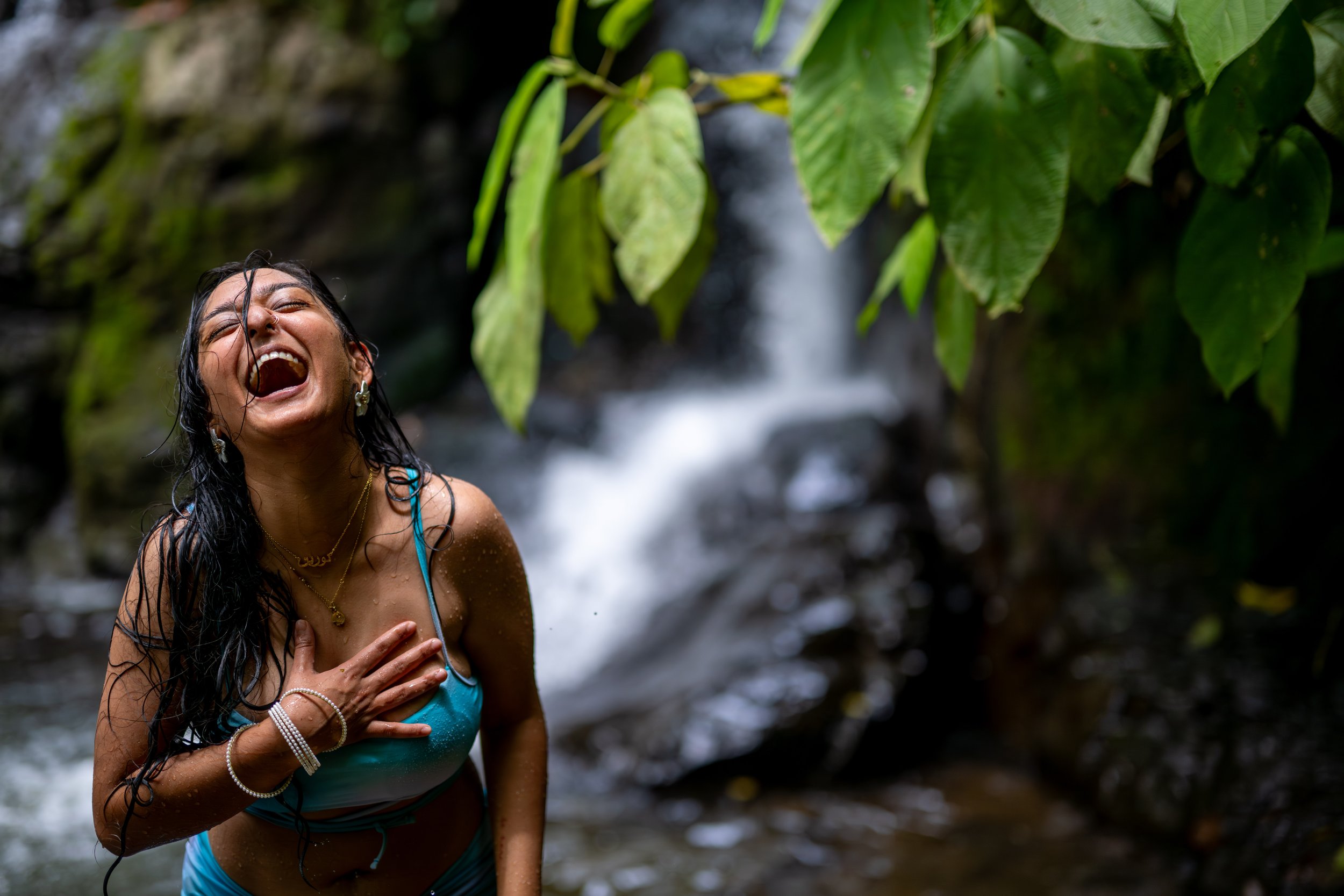 A woman enjoying herself in a waterfall in a lush, green jungle with water droplets on her skin and wet hair.