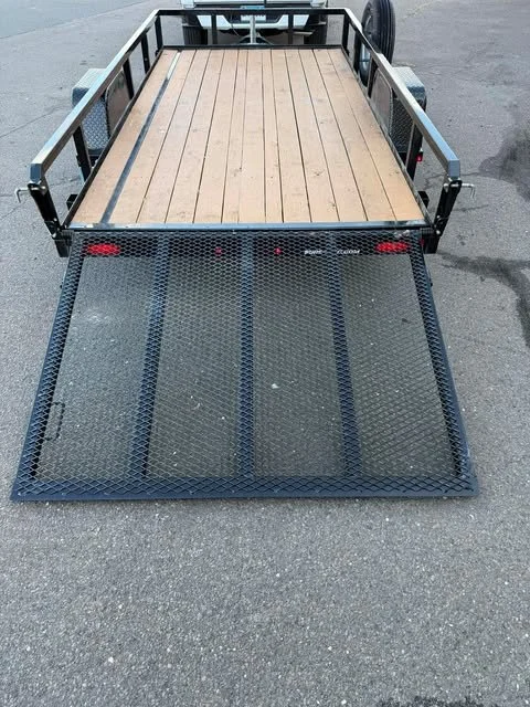 Cargo trailer with a wooden floor and a foldable metal ramp at the back, parked on asphalt pavement.