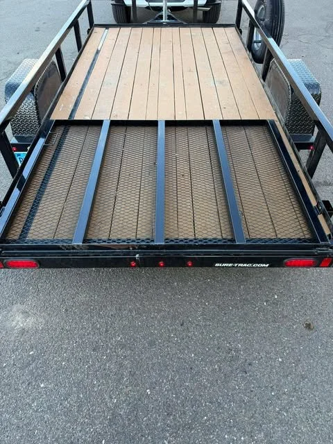 The back of a utility trailer with a wooden deck on one side and a metal mesh platform on the other, parked on asphalt.