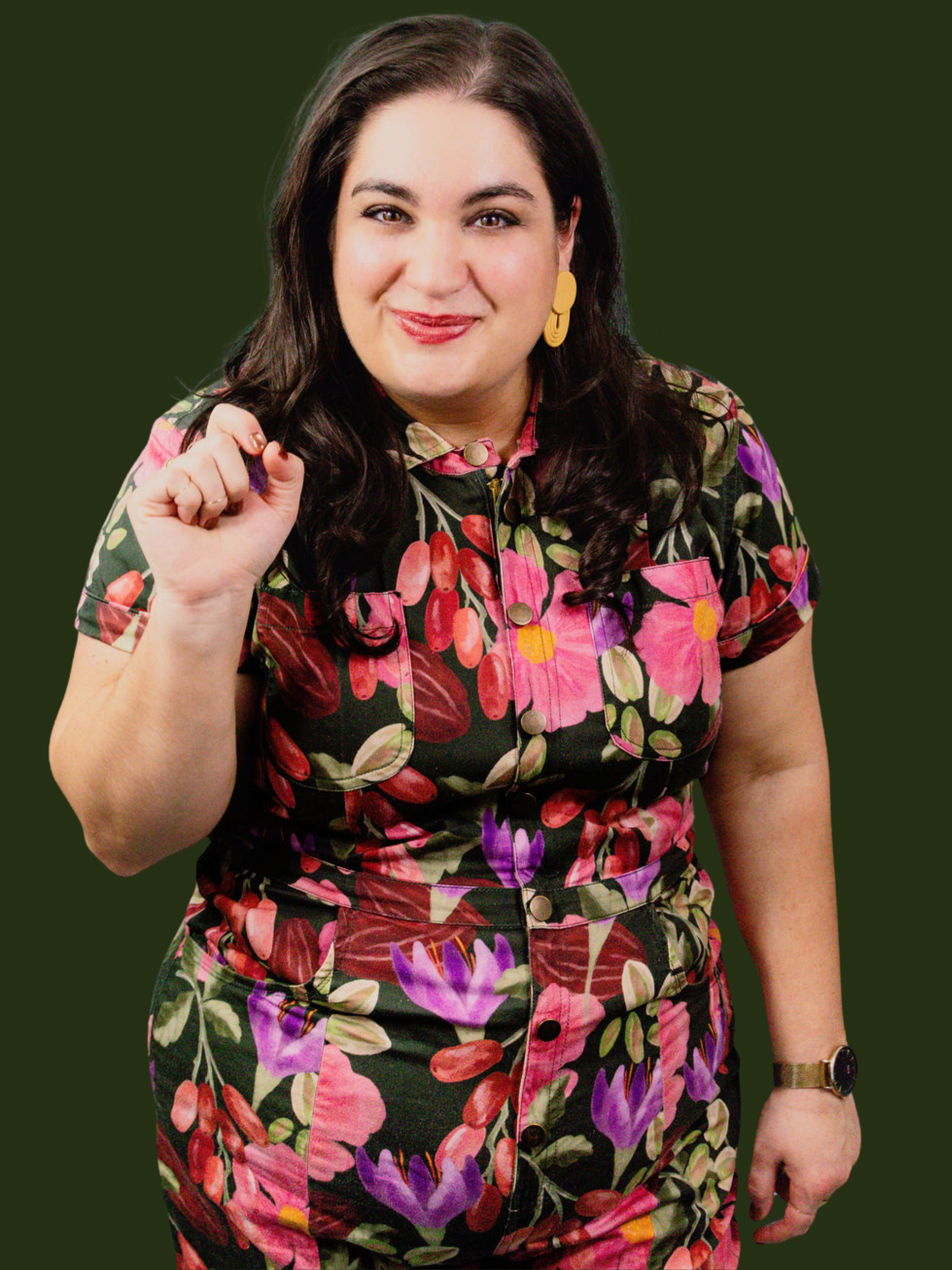 A woman with dark brown hair and earrings wearing a floral jumpsuit, smiling and raising her right fist.