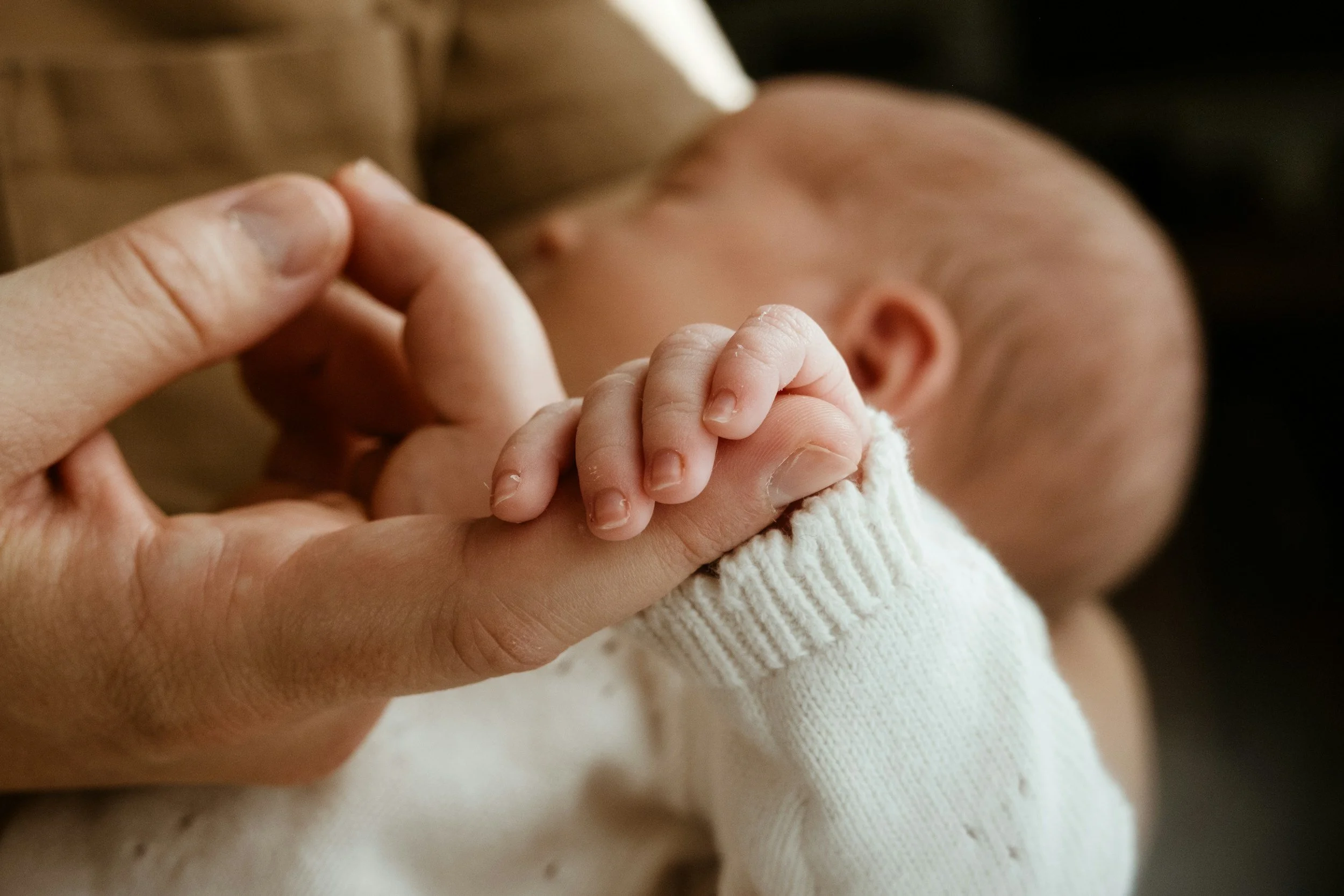 Close-up of an adult holding a baby's tiny hand, with the baby's face slightly blurred in the background.