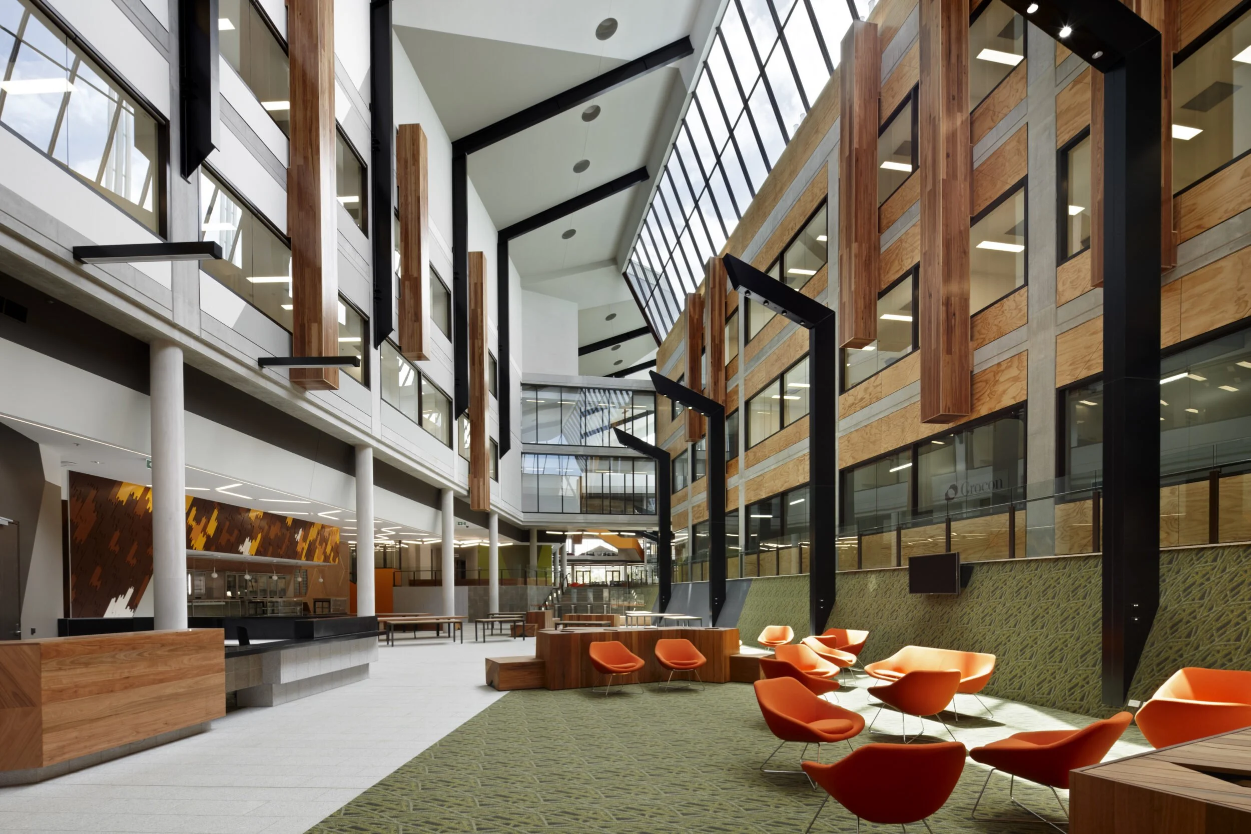 Interior view of a modern, spacious office lobby with orange chairs, green carpet, and large windows with black framing.