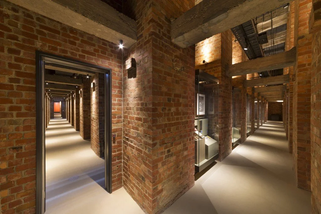 Long hallways with exposed brick walls, modern lighting, and display cases, resembling an art gallery or museum interior.