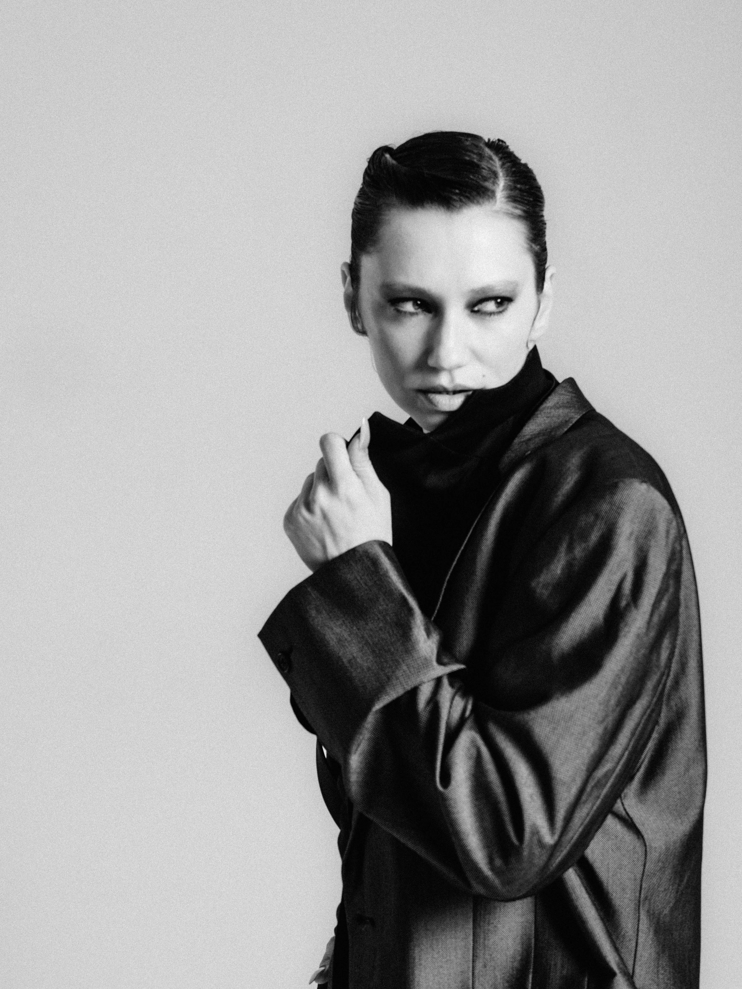 Black and white photo of a woman with short dark hair, wearing a blazer or jacket, looking to the side with a serious expression.